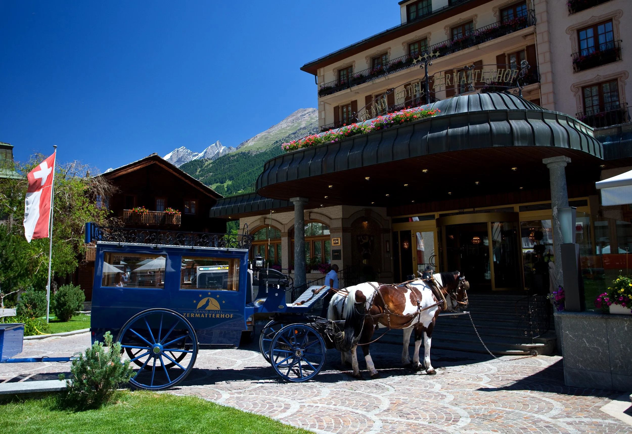 Horse-drawn carriage waiting outside the historic Grand Hotel Zermatterhof in the car-free centre of Zermatt.