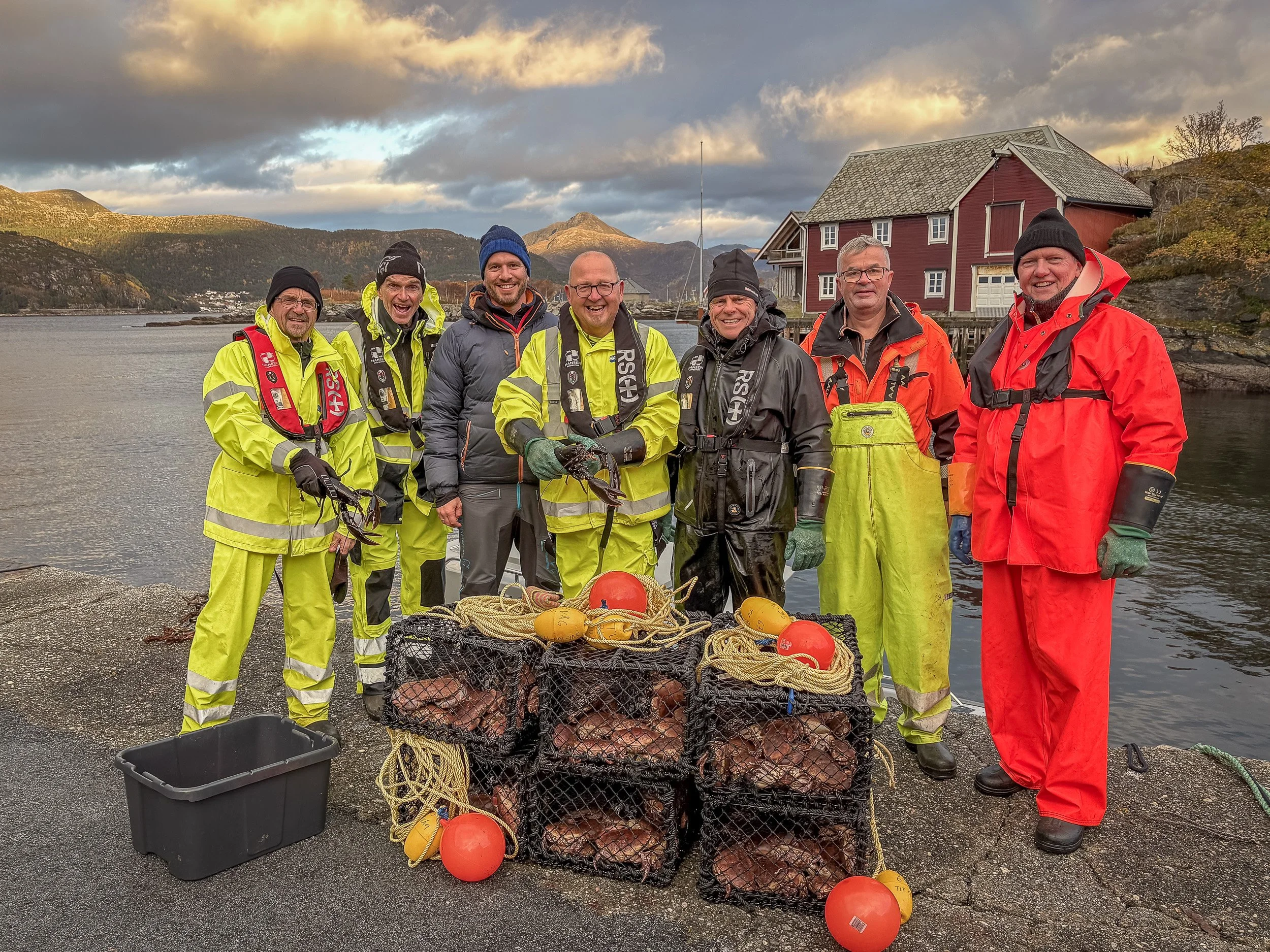 Krabbe- og hummerfiske i Husevåg – en blid gjeng på kaia med fulle teiner, omgitt av fjord, fjell og rorbuer i varmt kveldslys.