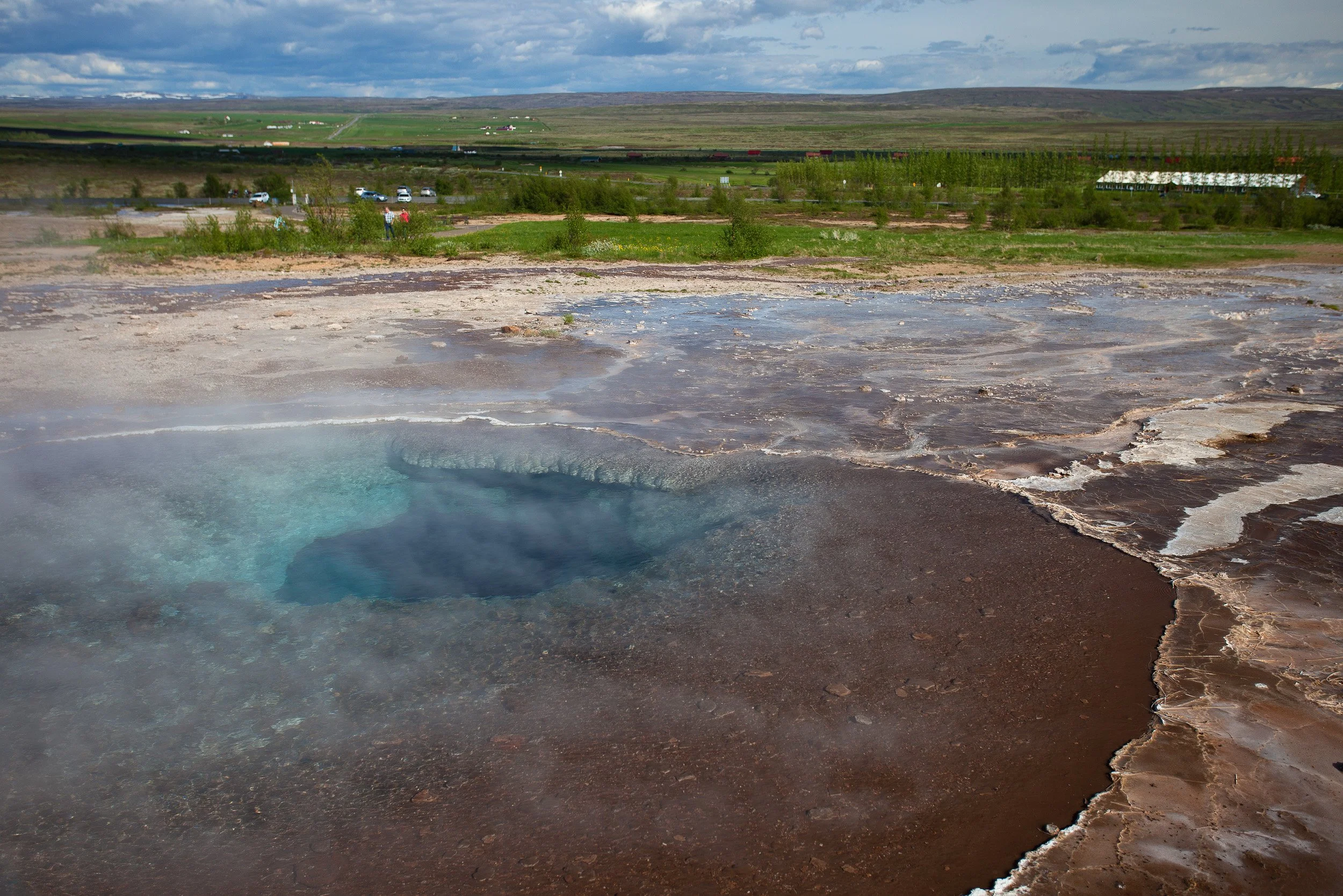 Strokkur’s hot pool simmers and swirls in mineral-blue tones, steam drifting over rust-coloured earth as the next eruption builds beneath the surface