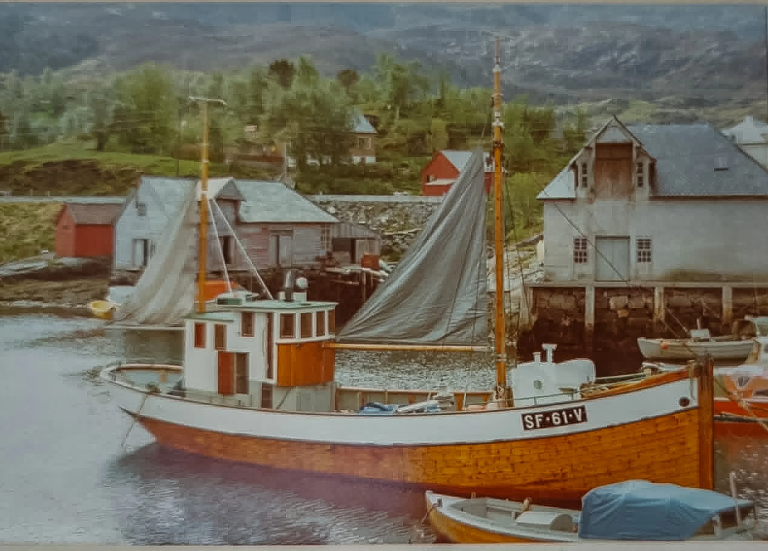 Historisk fargebilde av motorkutteren «Strandholm», merket SF-61-V, ved moloen i Husevåg med sjøhus og naust i bakgrunnen.
