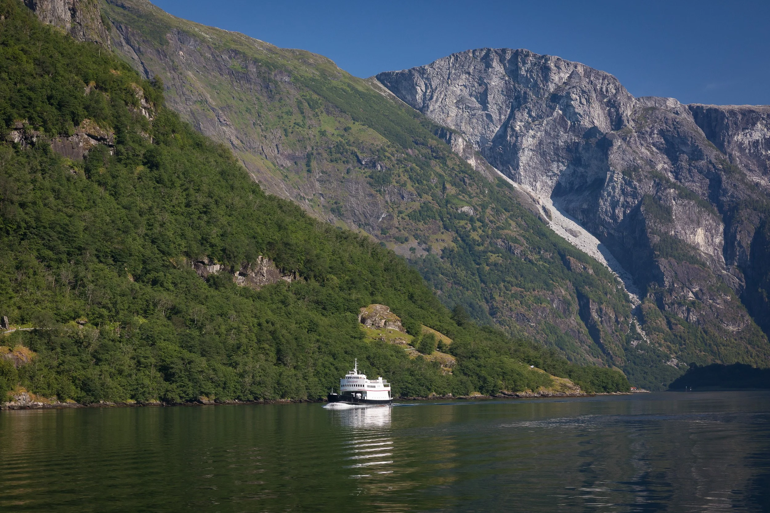A long, cinematic view through Nærøyfjorden, where the fjord narrows into a dramatic corridor of green slopes and rock.