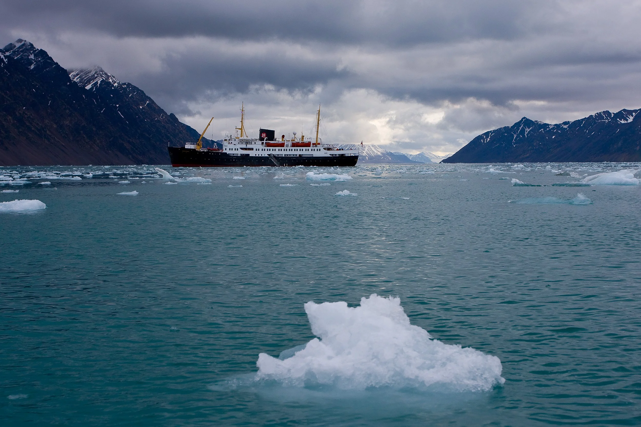 The expedition ship moves through broken ice near Lilliehöökbreen, dwarfed by the scale of the fjord.