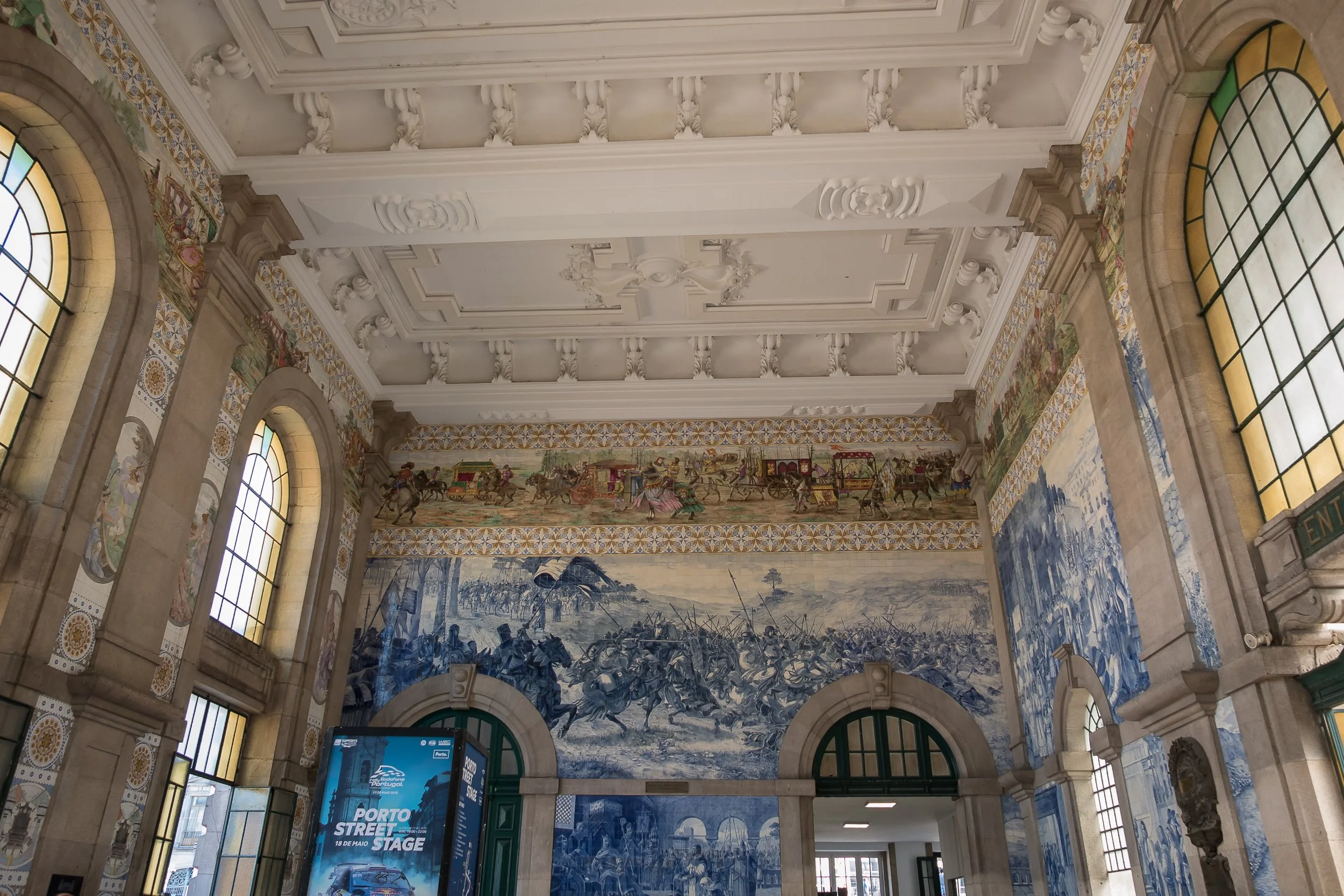 The azulejo-covered hall of São Bento railway station in Porto, with historic blue tile panels rising beneath the ornate ceiling.