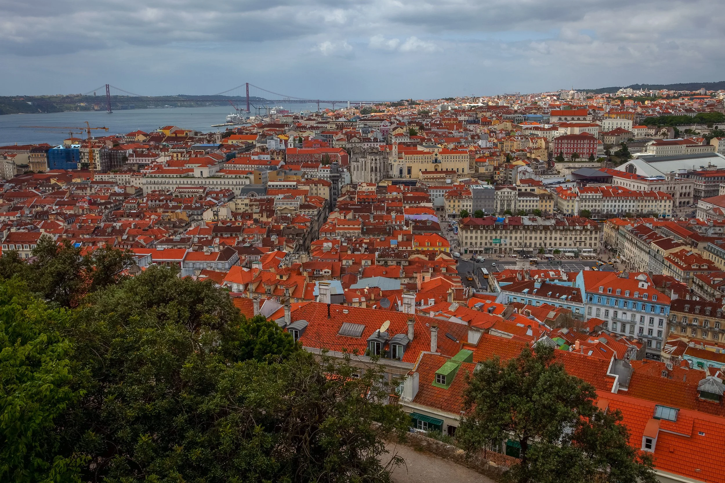 Lisbon’s red rooftops stretch towards the Tagus River and the 25 de Abril Bridge, seen from one of the city’s hilltop viewpoints.