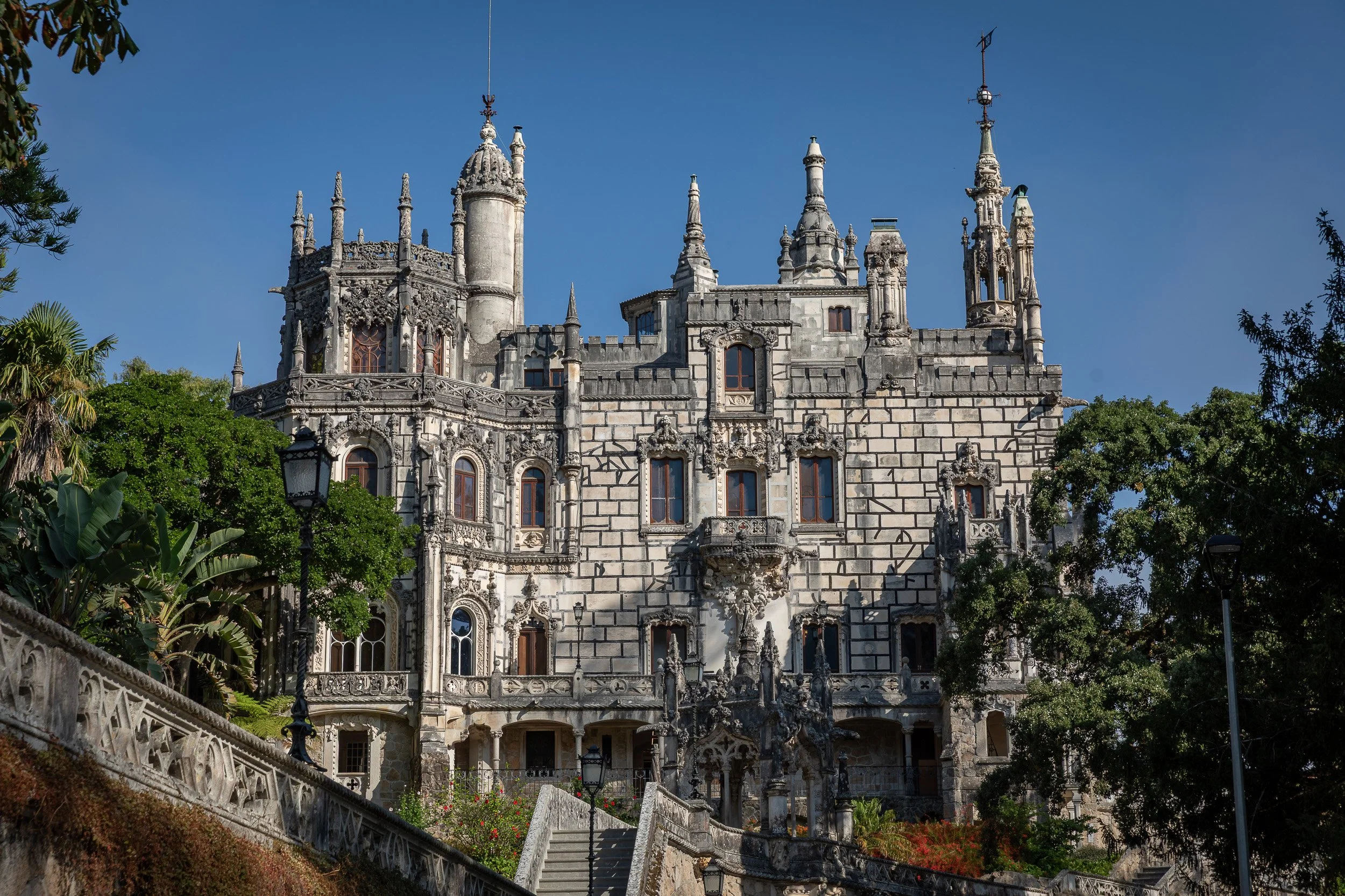 Quinta da Regaleira in Sintra, with its ornate façade, towers and garden paths set against a deep blue sky.
