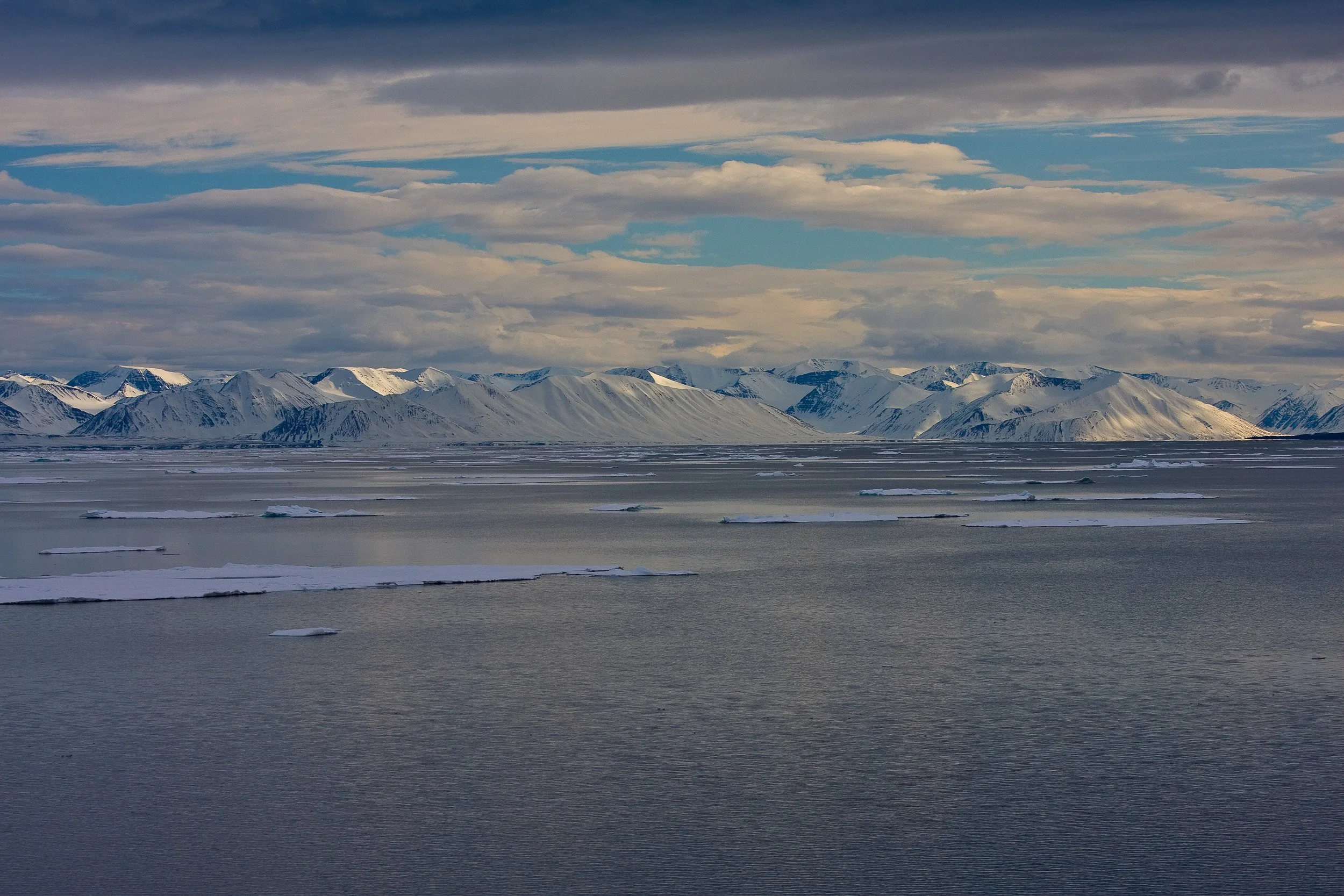Snow-covered ridges at 80 degrees north stretch across the horizon beneath a layered northern sky.