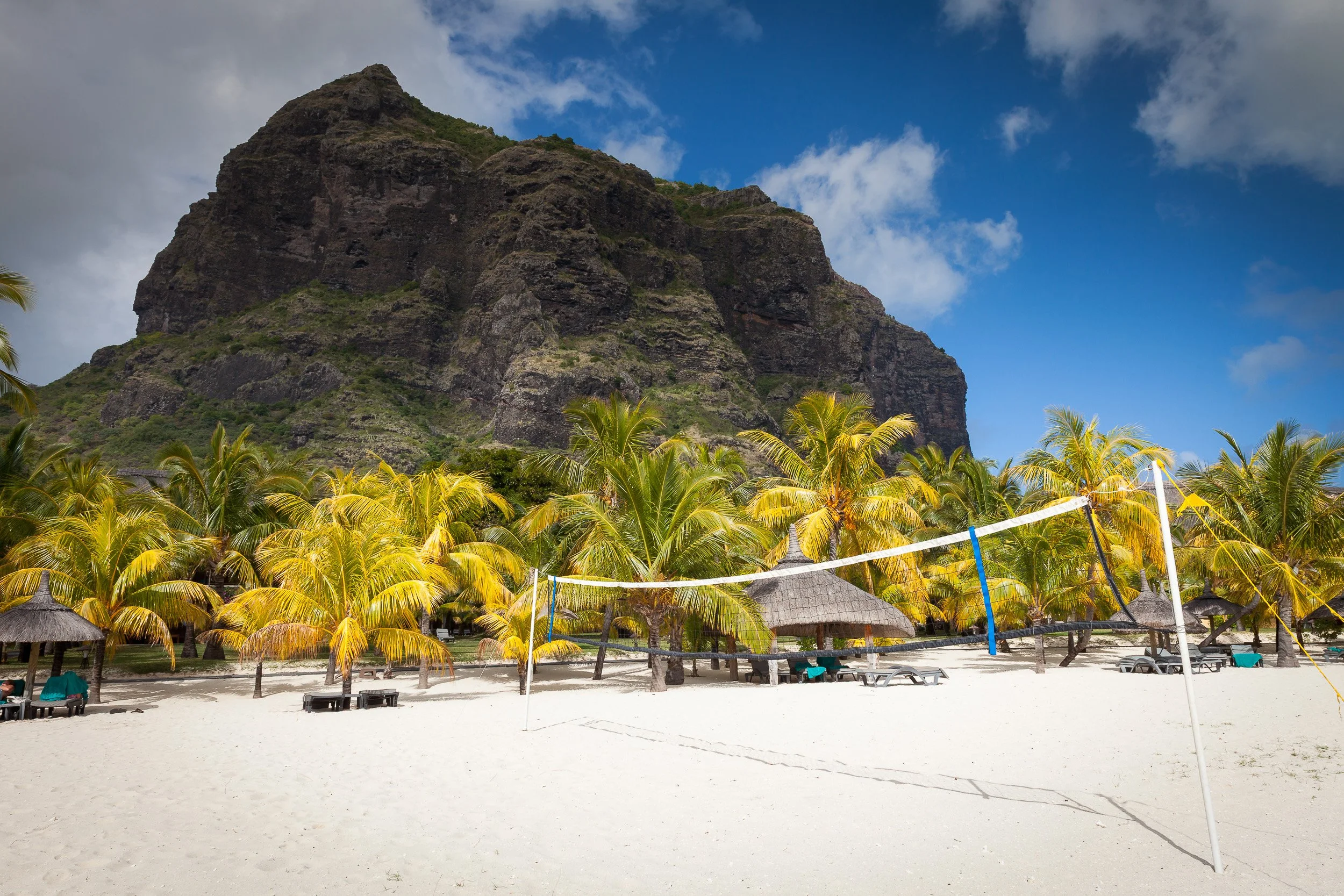 Sandy beach volleyball court at Le Morne, Mauritius, set between golden palm trees and the dramatic cliffs of Le Morne Brabant.