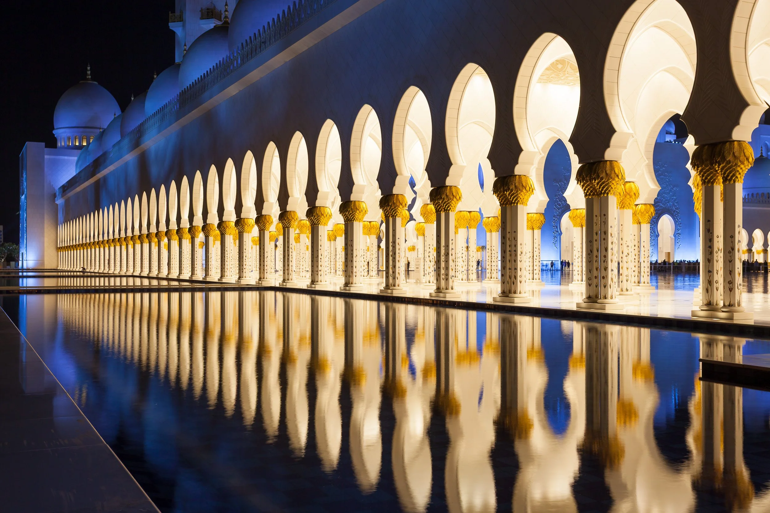 A luminous colonnade and still water reflecting the elegance of Sheikh Zayed Grand Mosque, Abu Dhabi.