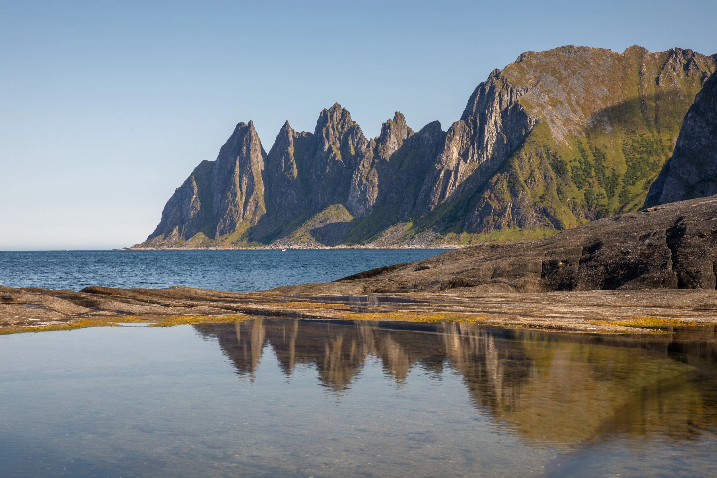 The Okshornan peaks reflected in a calm rock pool at Tungeneset, where polished coastal stone meets the open Norwegian Sea.