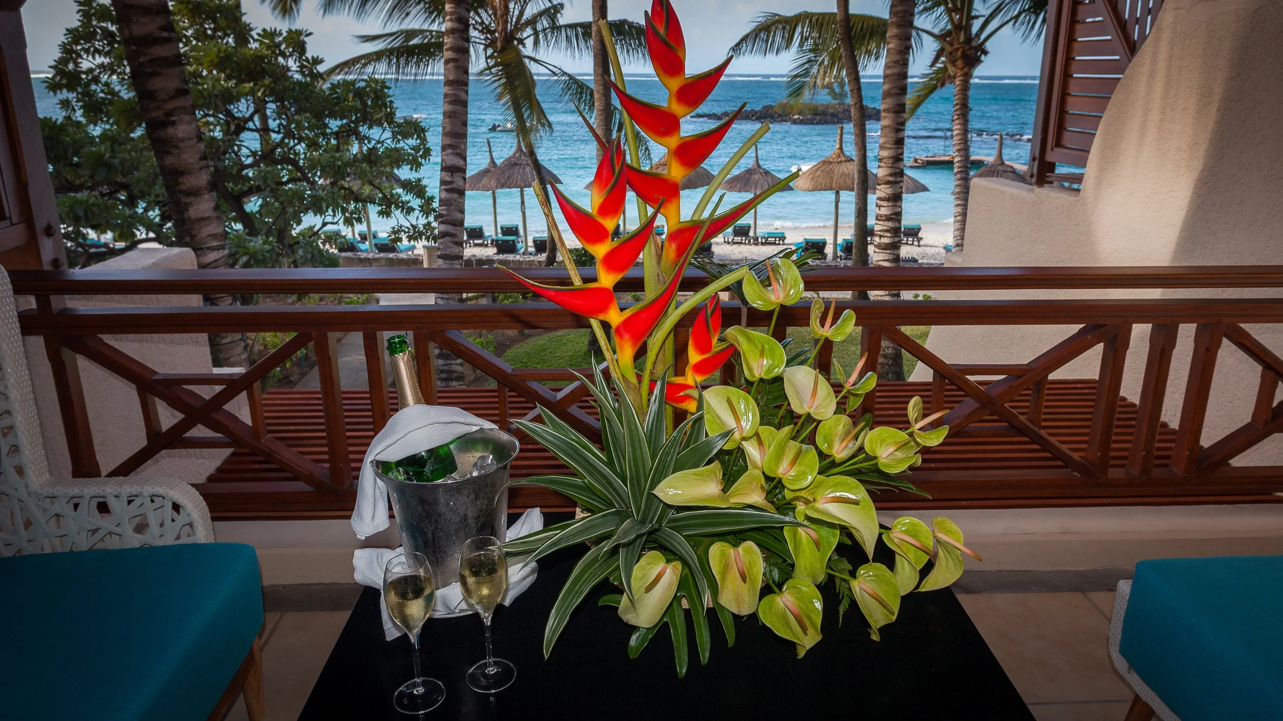 Welcome arrangement of tropical flowers and chilled champagne on a balcony at Constance Belle Mare Plage, with the beach and palms below.