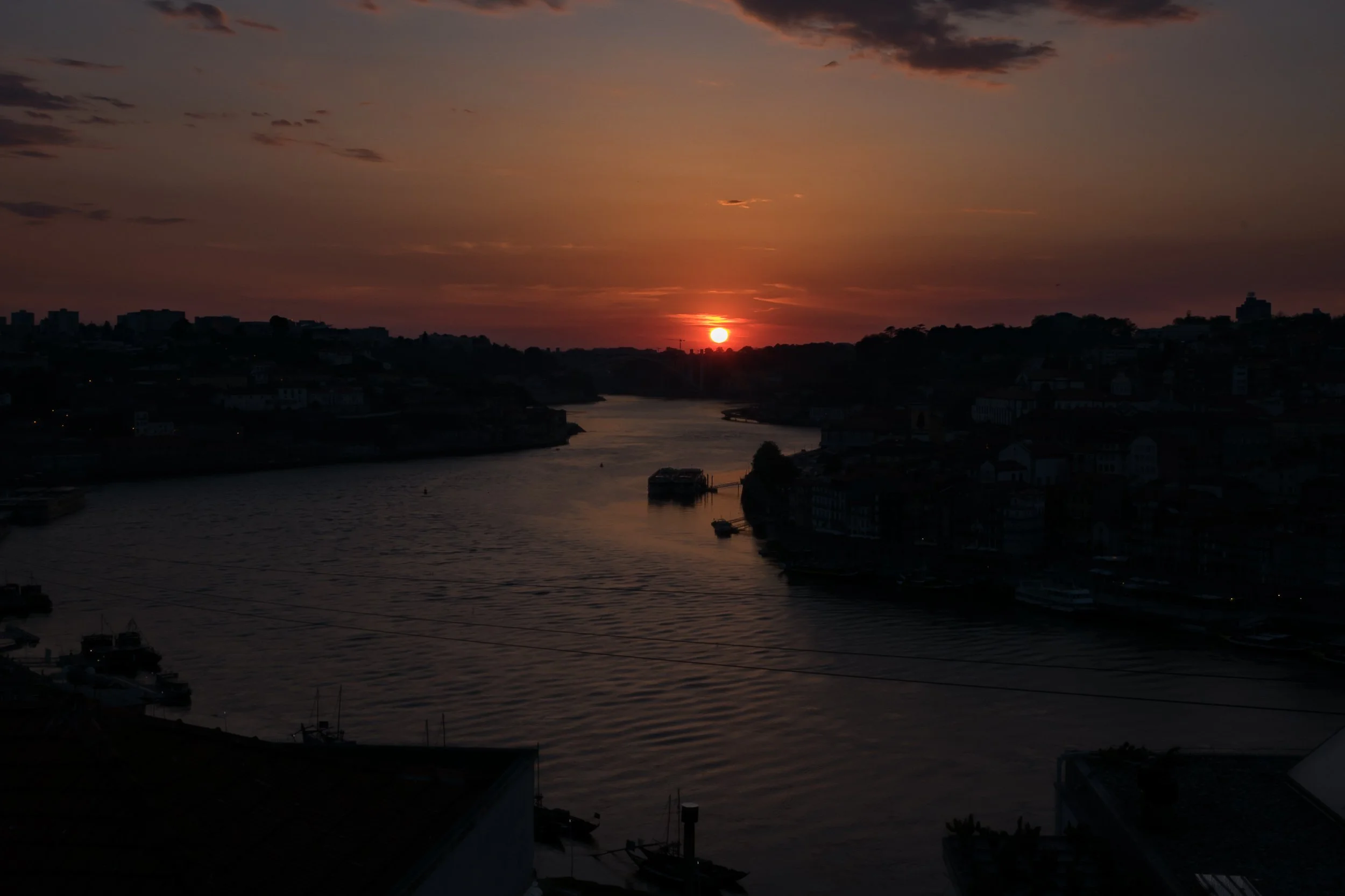 Sunset over the Douro River in Porto, with the city reduced to silhouettes around the last red light on the horizon.