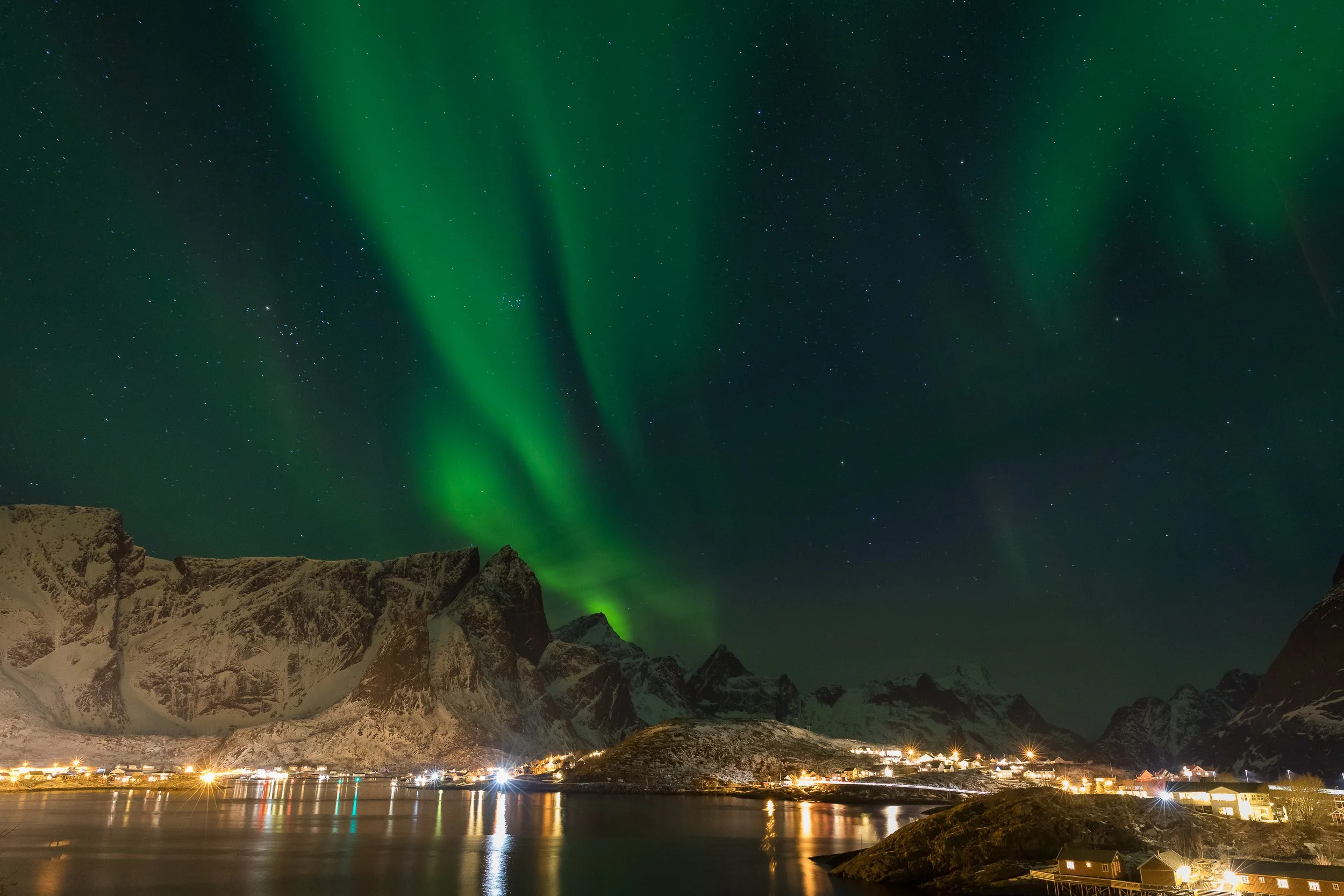 Northern lights (aurora borealis) in Reine, Lofoten Islands, Norway – aurora dancing above fjord, cabins and mountains.