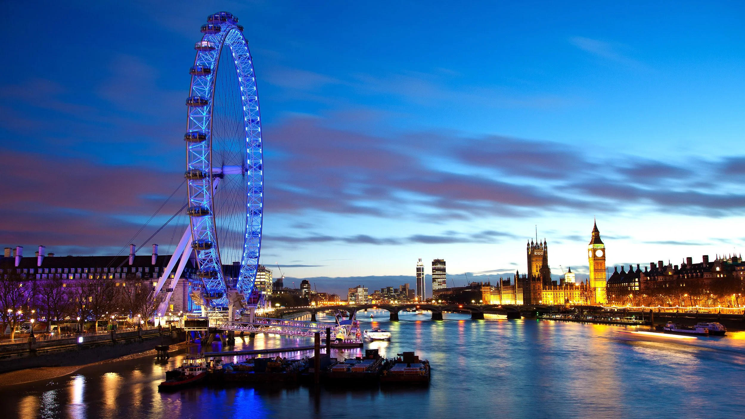 The London Eye at night in London, UK – glowing Ferris wheel spinning above the Thames in a long-exposure cityscape.