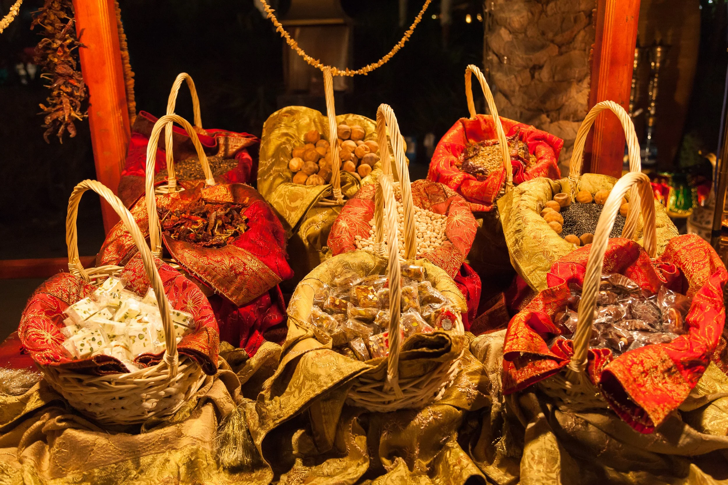 Baskets of sweets, nuts and dried fruits presented in rich fabrics at a lavish Dubai display.