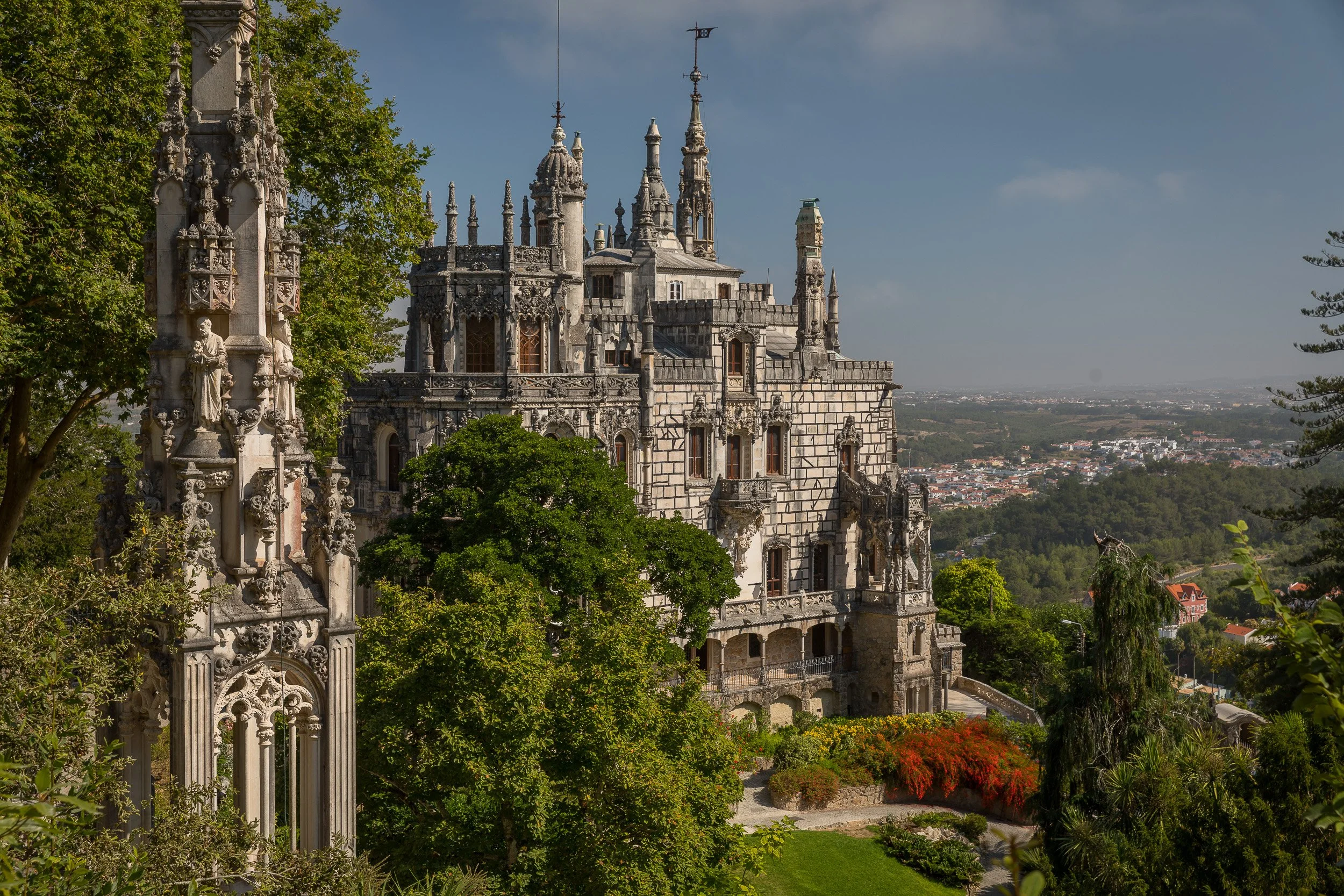 Quinta da Regaleira seen from the gardens, with Gothic towers, dense greenery and the Sintra landscape stretching into the distance.