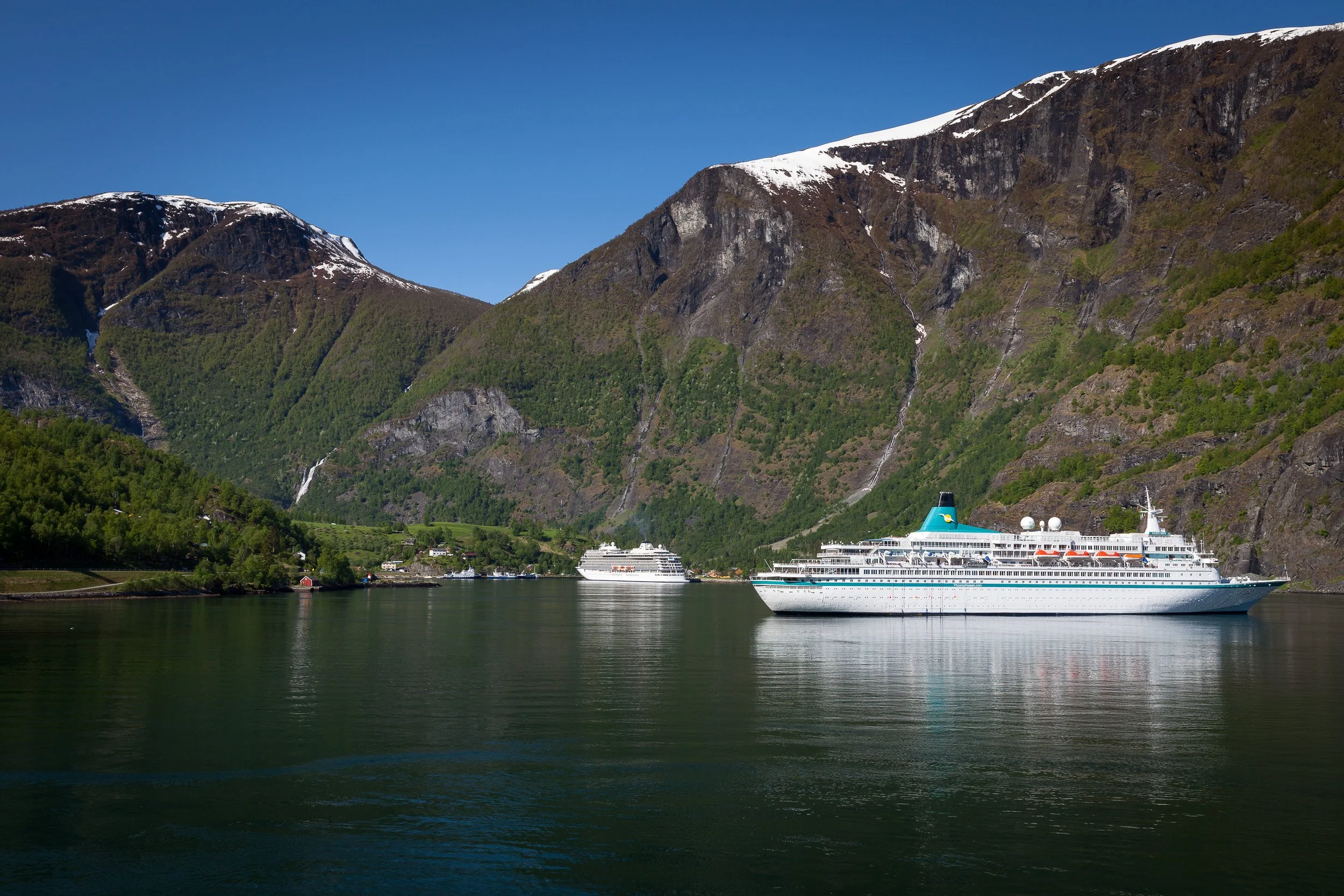 Flåm on the shore of Aurlandsfjord — a tiny village dwarfed by steep mountains and thin waterfalls, and a classic stop on Norway’s fjord cruises.