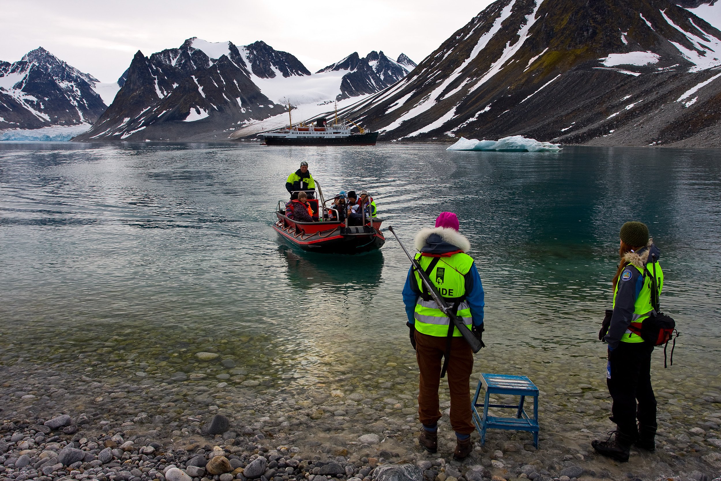 A Zodiac returns to shore in Magdalenefjorden, with guides, glacier water and the expedition ship backed by sharp Arctic peaks.