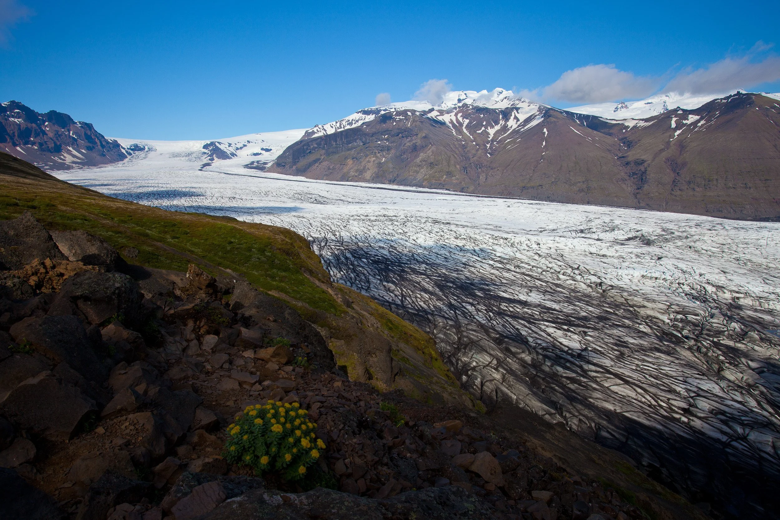 A sweeping Skaftafellsjökull glacier tongue streaked with volcanic ash, spilling from the high ice cap into the mountains under crisp blue skies.