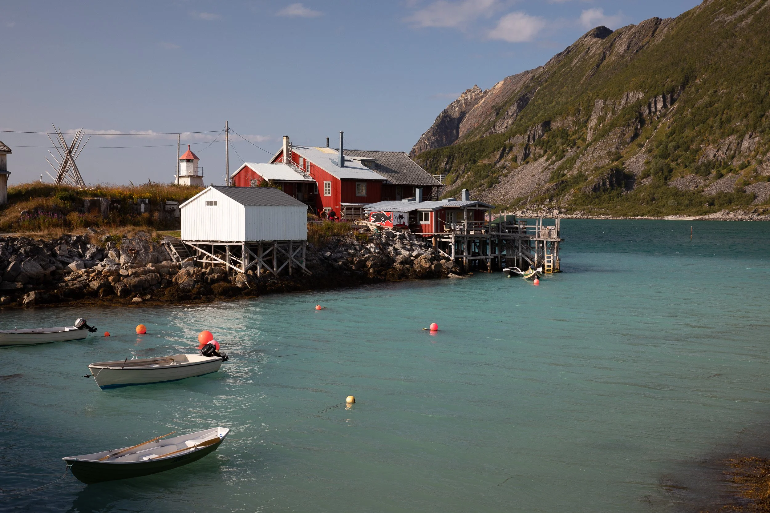 Clear turquoise water, small boats and red coastal buildings at Bøvær, where Senja’s fishing heritage sits beneath steep mountains.