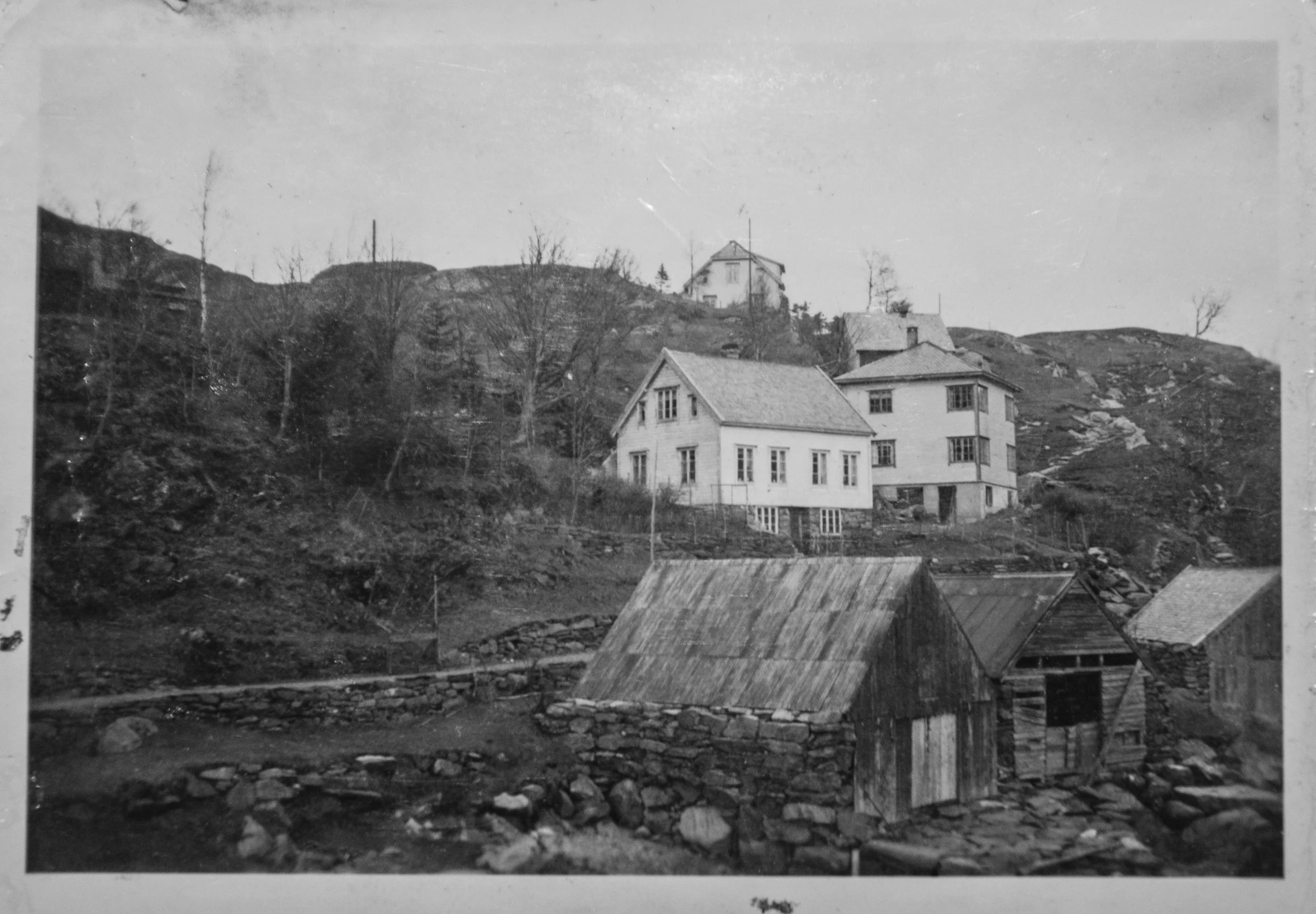 Historisk svart-hvittbilde fra Vågen i Husevåg, med sjøhus og naust ved sjøen og eldre bolighus i dalsiden bak.
