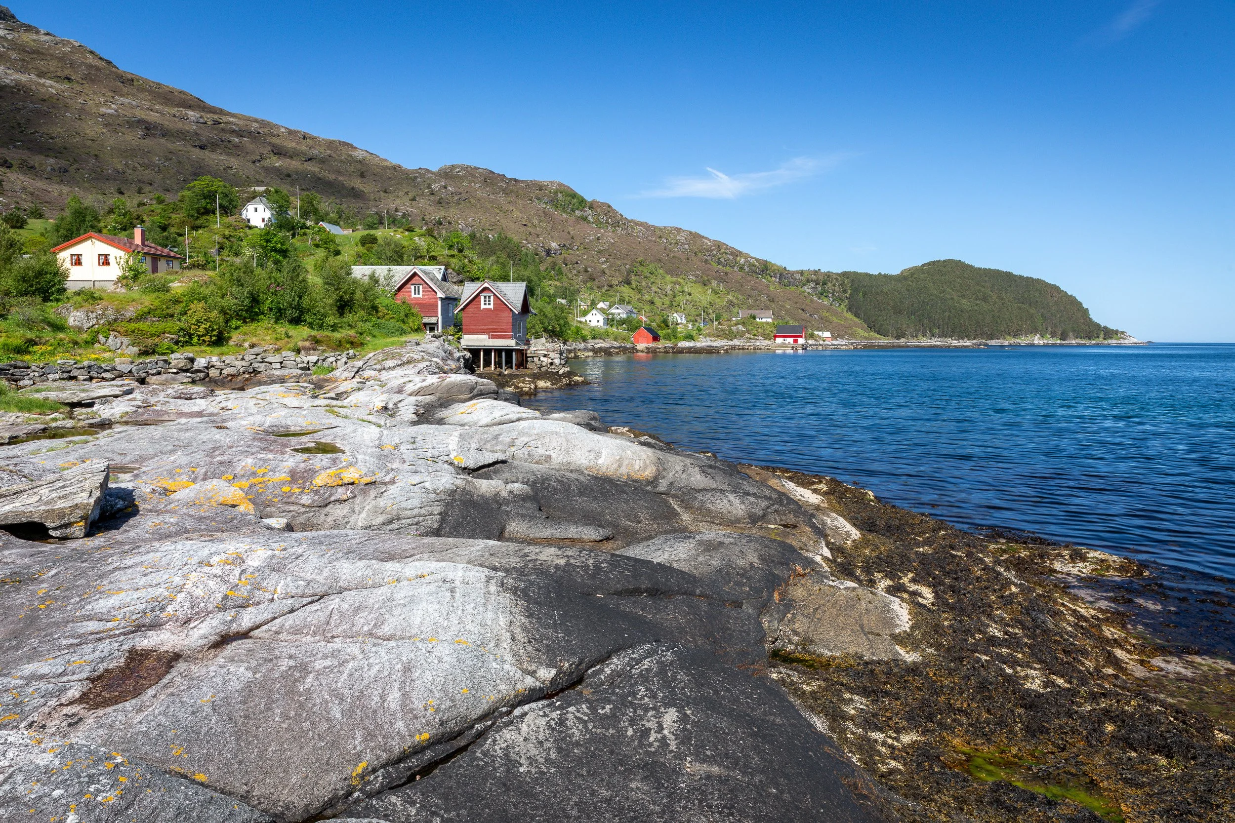 Svaberg ved elveosen i Husevåg, i området der fisk tidligere ble lagt til tørk på bergene. Sjøhusene, fjorden og den åpne kystlinjen viser hvordan bygda har vært tett knyttet til sjøen og fisket.