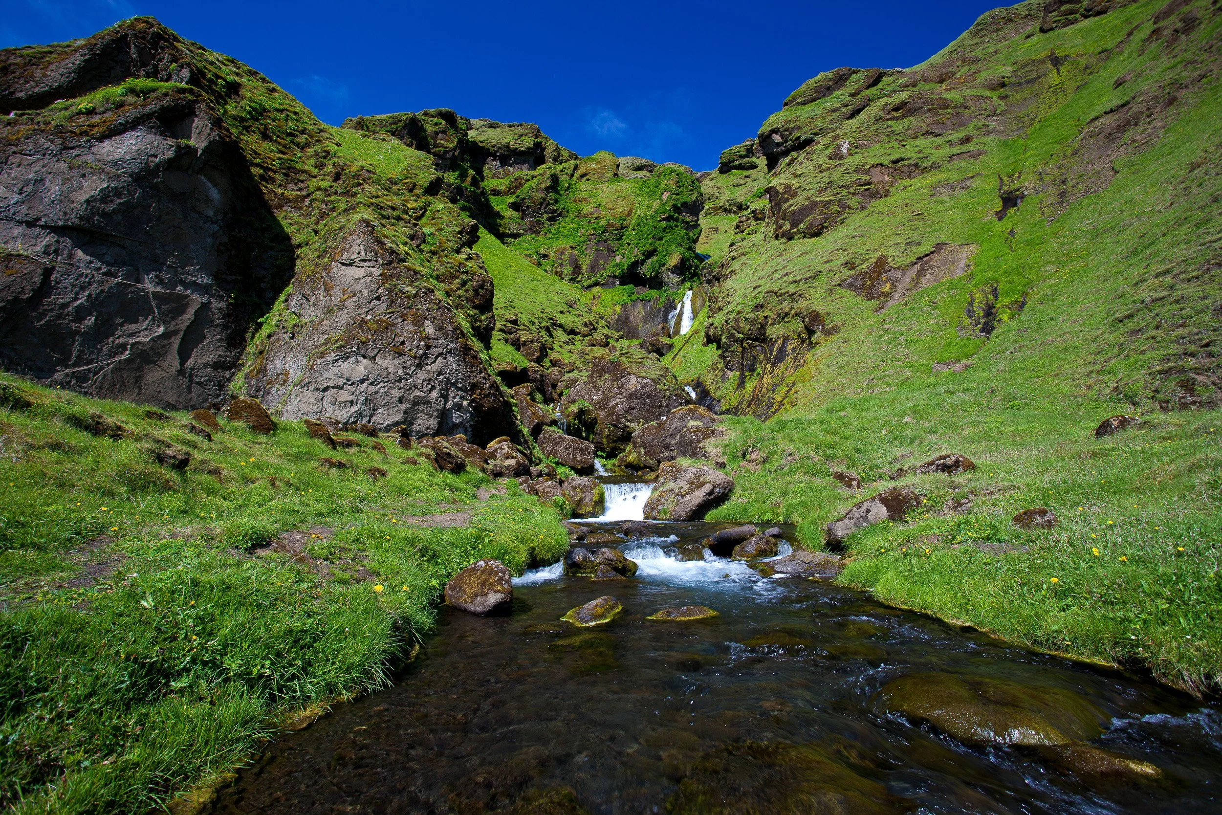 Uxafótafoss — a small waterfall and stream threading through bright mossy slopes, Iceland’s greenery hiding the volcanic bones below.