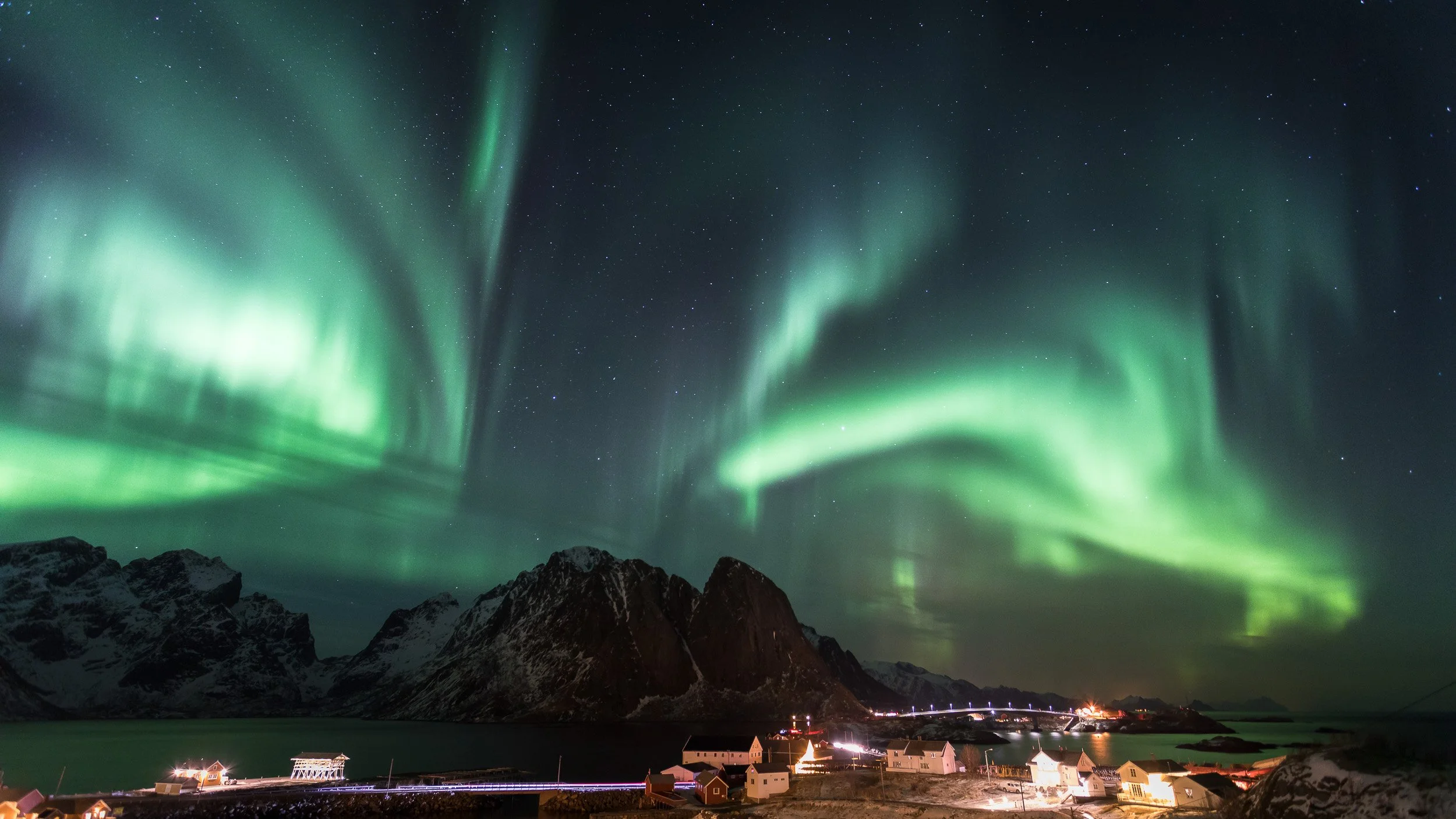 Northern Lights over Reine in Lofoten, Norway – fishing village, red cabins and jagged peaks under a glowing aurora sky. One of my favourite aurora scenes in Lofoten.