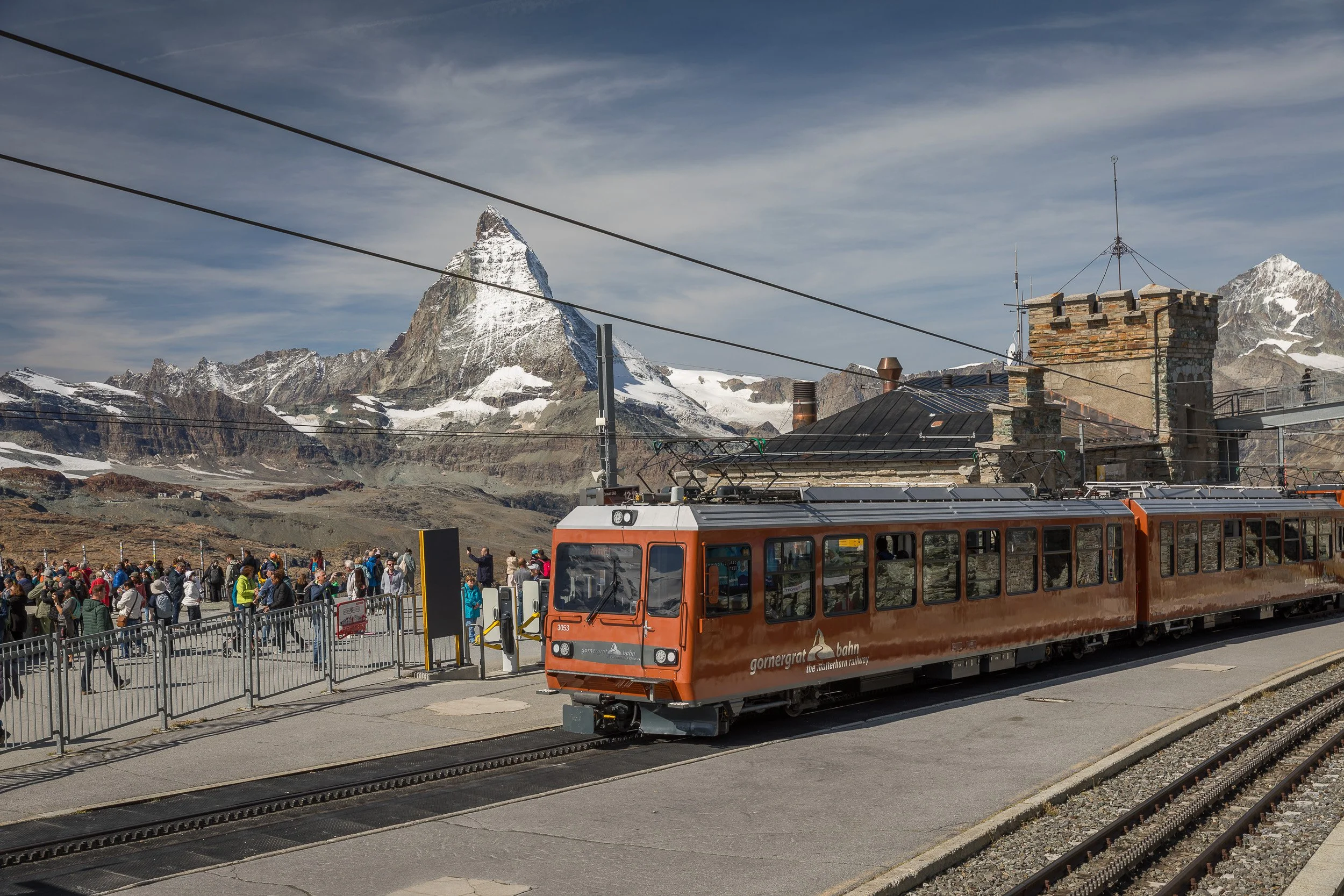 Crowds at the Gornergrat summit station as the orange cogwheel train arrives, with the Matterhorn towering in the background.