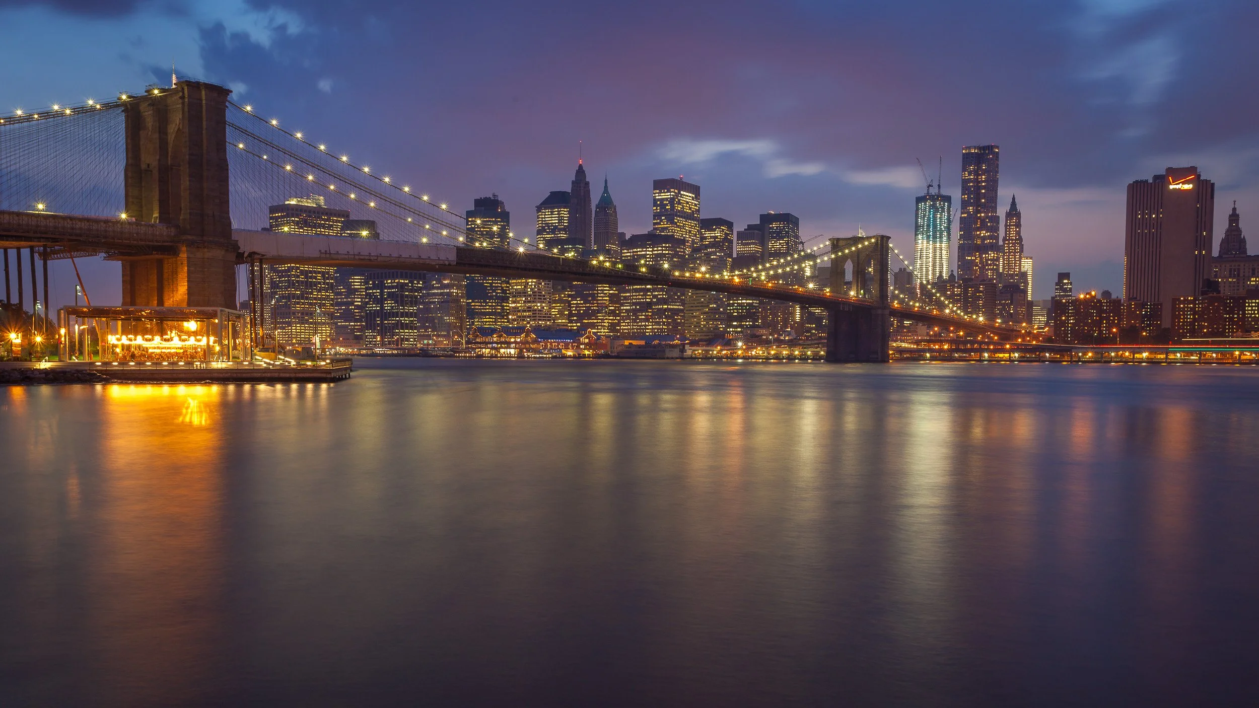 Brooklyn Bridge and Lower Manhattan at blue hour in New York City, USA – bridge lights, skyline windows and soft reflections across the East River.