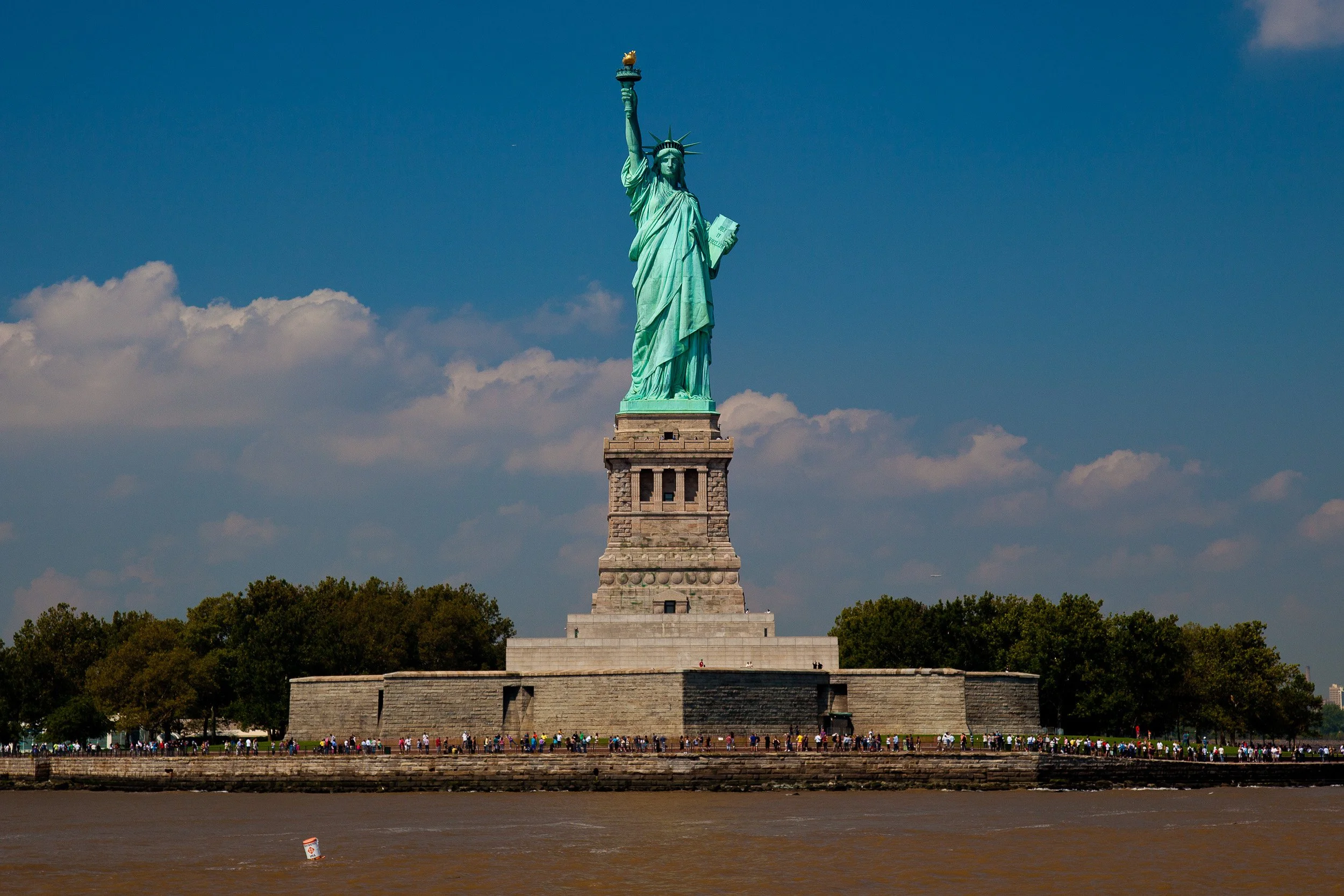 The Statue of Liberty standing proud beneath a deep blue sky and drifting cloud banks.