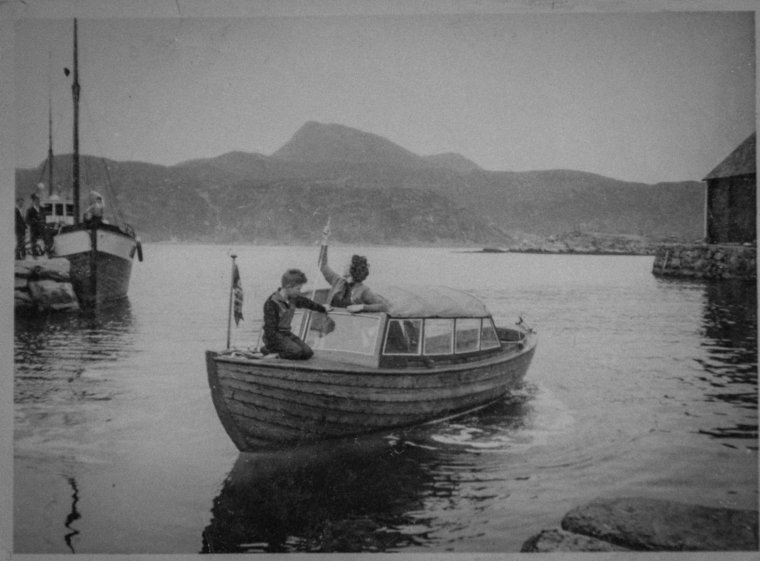 M/B «Grete» SF-185-D i Husevåg, ca. 1961 – en 22 fot lang og 7 fot bred tresnekke, bygget i 1947 og utstyrt med Marna 8 hk motor fra 1951. Bildet viser folk i båten på sjøen ved bygda, med en kutterbåt ved kai i bakgrunnen. Fotograf Svein Tunli. Kild