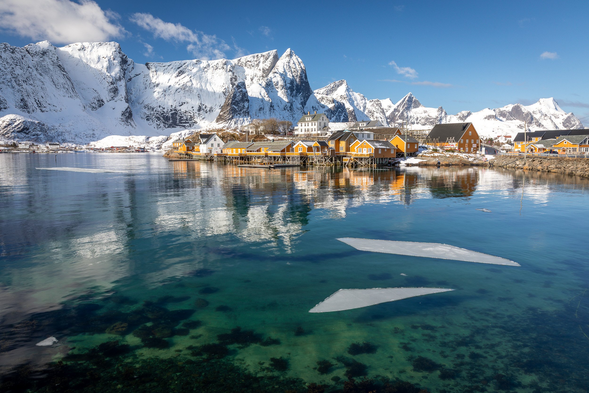Sakrisøy fishing village in the Lofoten Islands, Norway – yellow cabins on stilts between turquoise water and steep mountain peaks.
