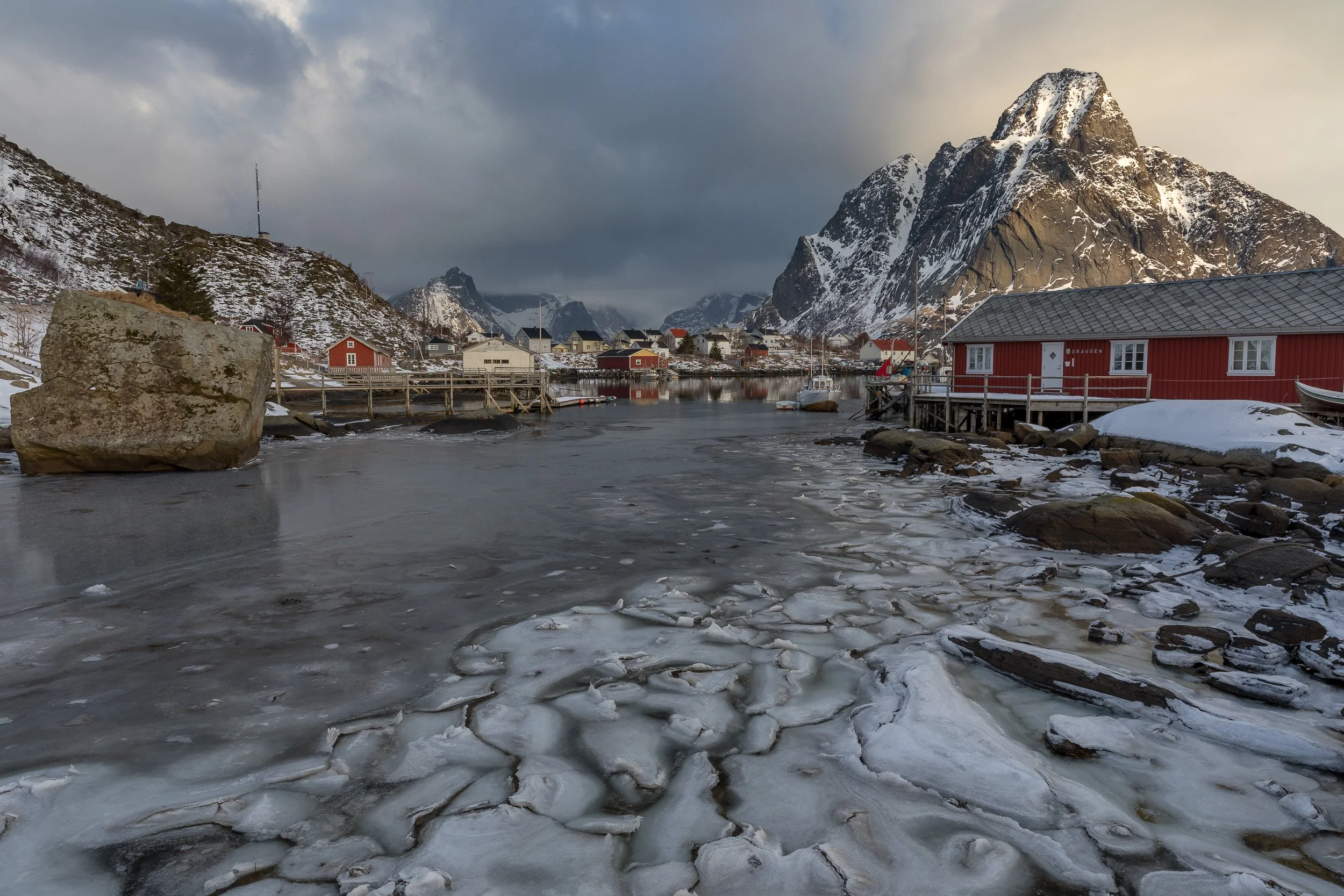 Winter in Reine in the Lofoten Islands, Norway – snow-covered cabins and mountains reflected in a cold, blue fjord.
