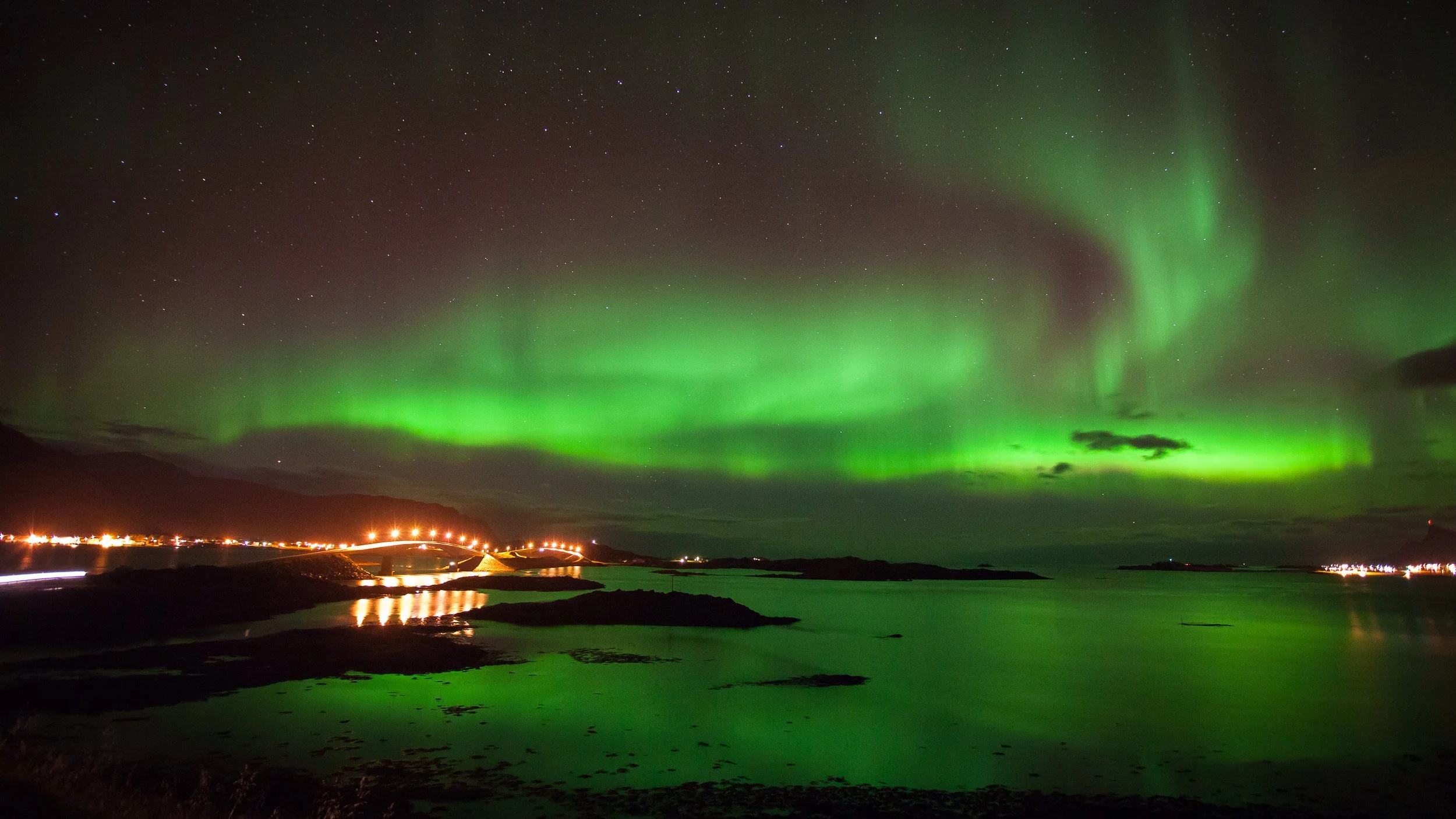 Northern Lights over the Fredvang Bridges in Lofoten, Norway – green aurora reflected in the dark sea between islands and Arctic mountain silhouettes.