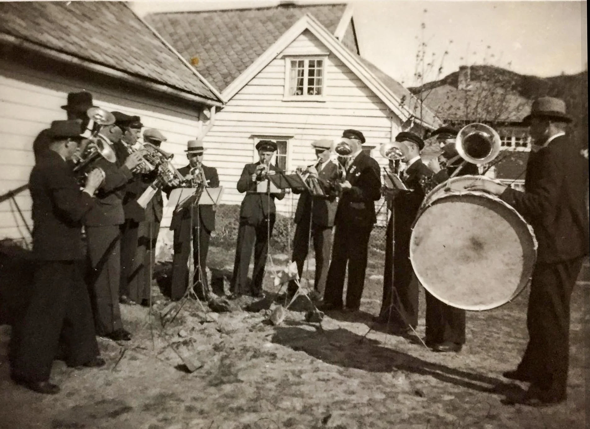 Husevåg hornmusikk utenfor skolehuset i Husevåg, 1947 – menn fra Husevåg samlet med blåseinstrumenter, stortromme og notestativer. Bildet viser skolehuset som mer enn en skolebygning; det var også en viktig samlingsplass for bygda og det lokale kultu