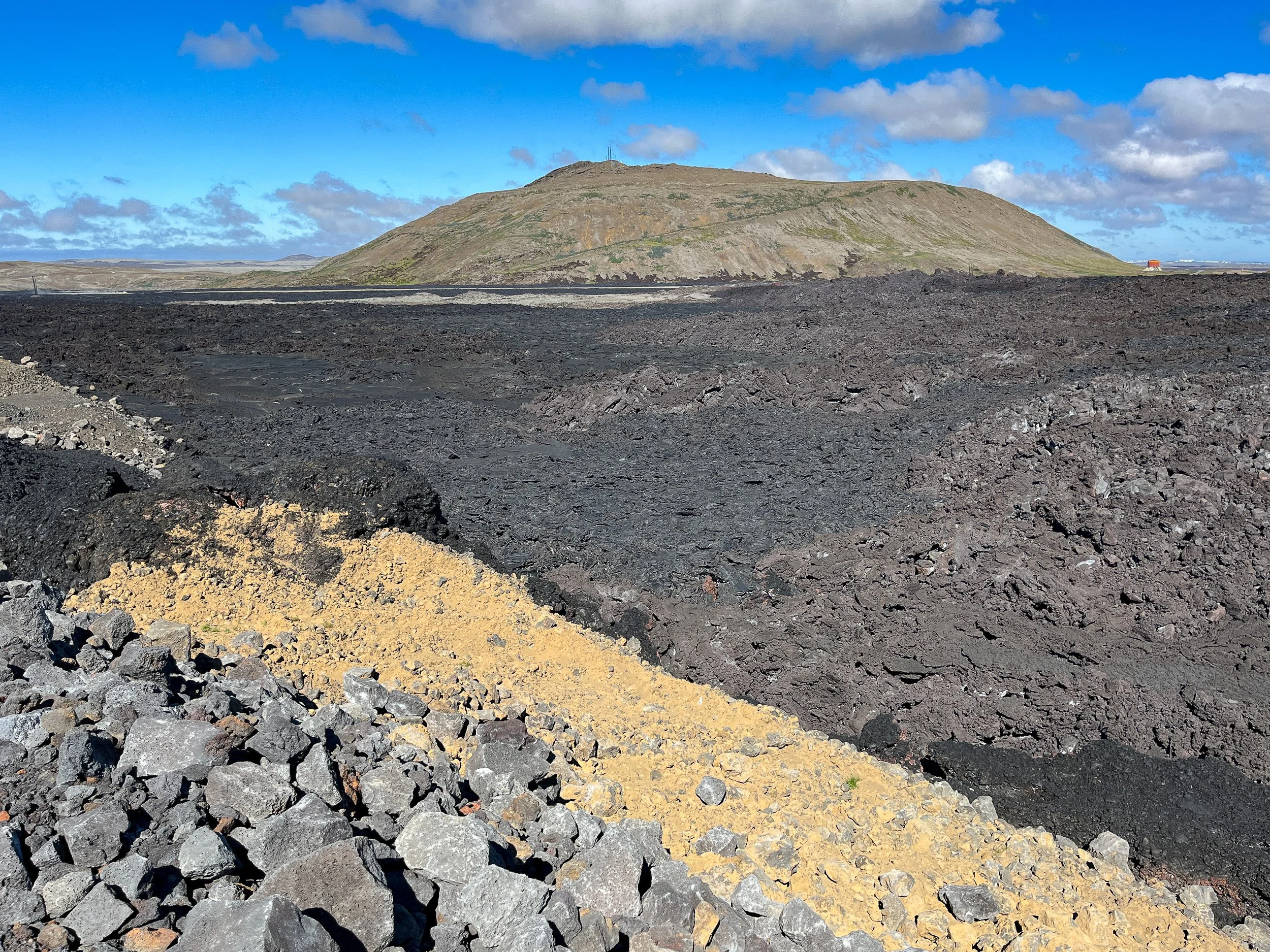 Volcanic landscape north of Grindavík, 2024 — raw, black lava spread across the ground, with a low ridge and open sky emphasising the aftermath.