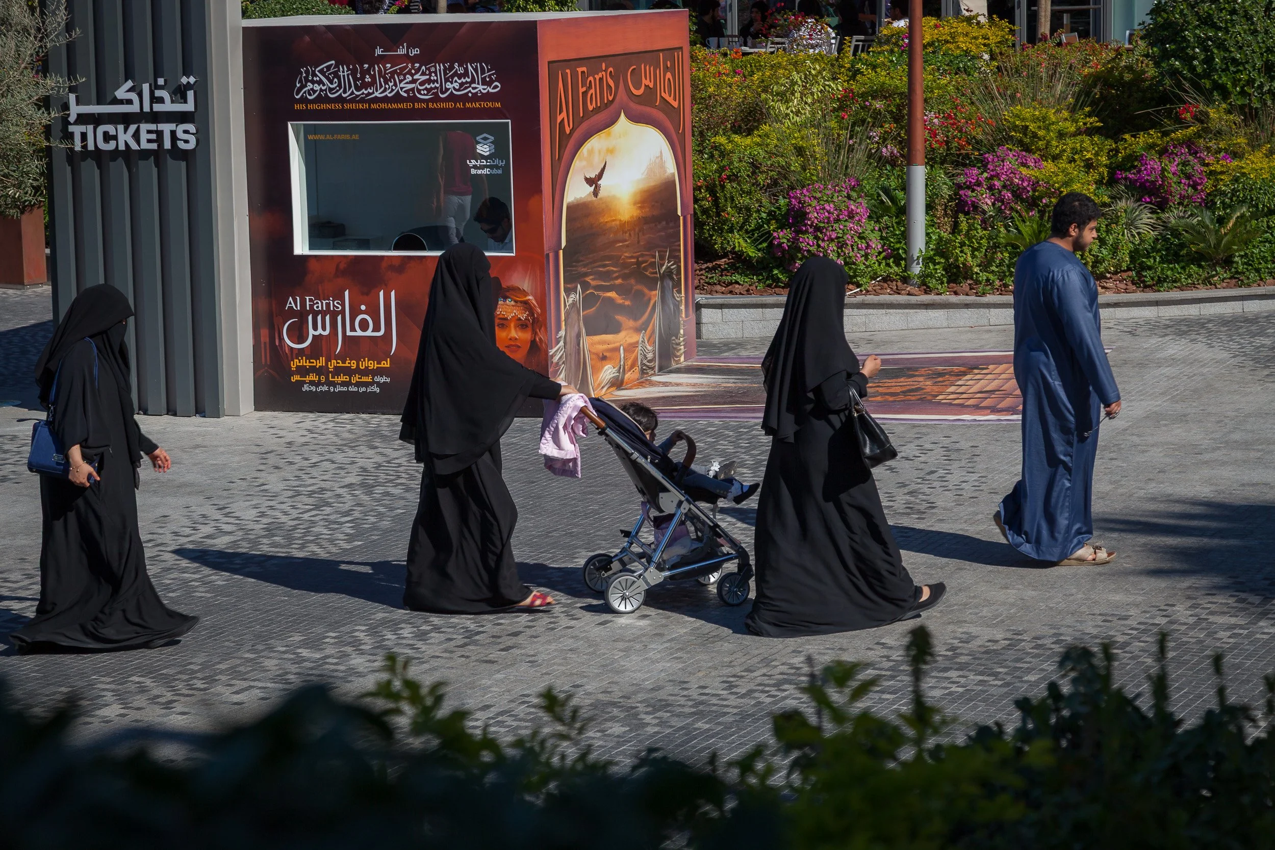 A candid street scene of daily life in Dubai, with traditional dress against a modern backdrop.