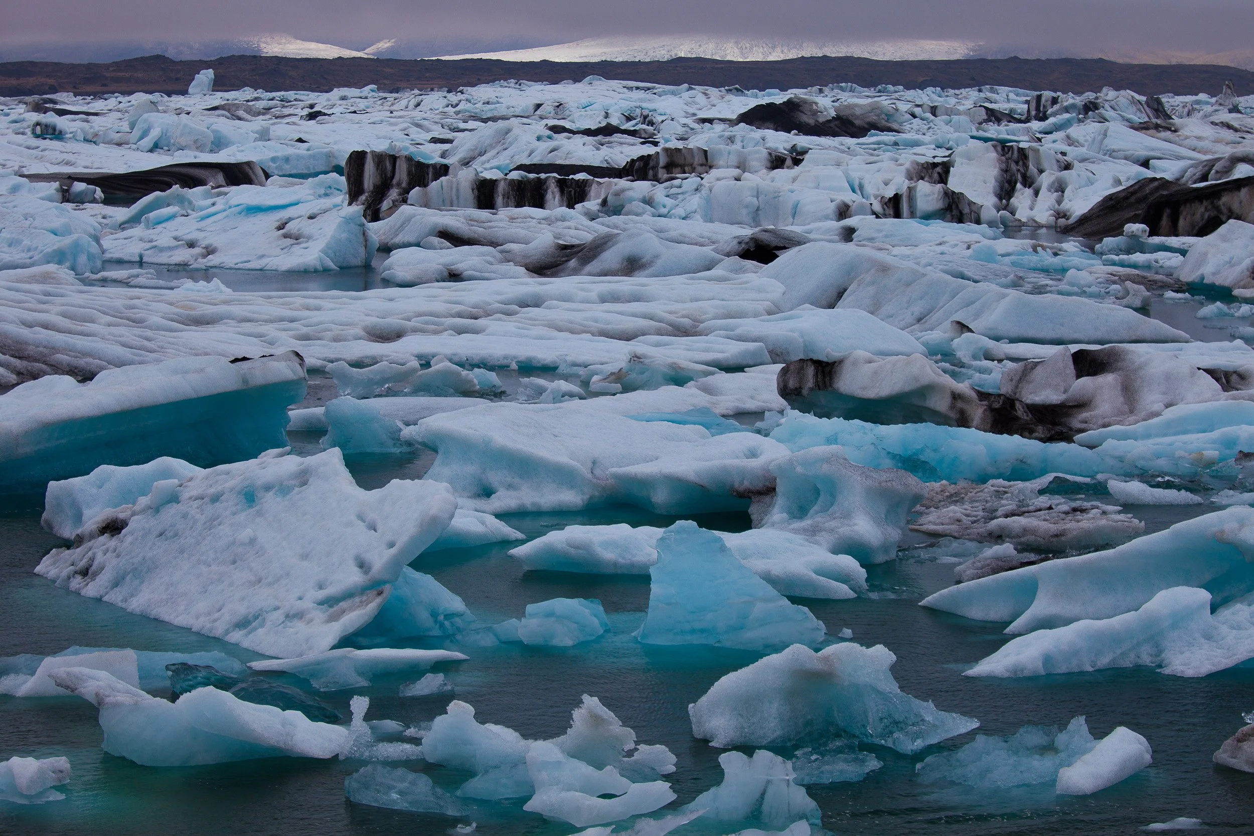 Jökulsárlón Glacier Lagoon, Iceland — a drifting mosaic of blue and white icebergs spreads across still water under a brooding sky.