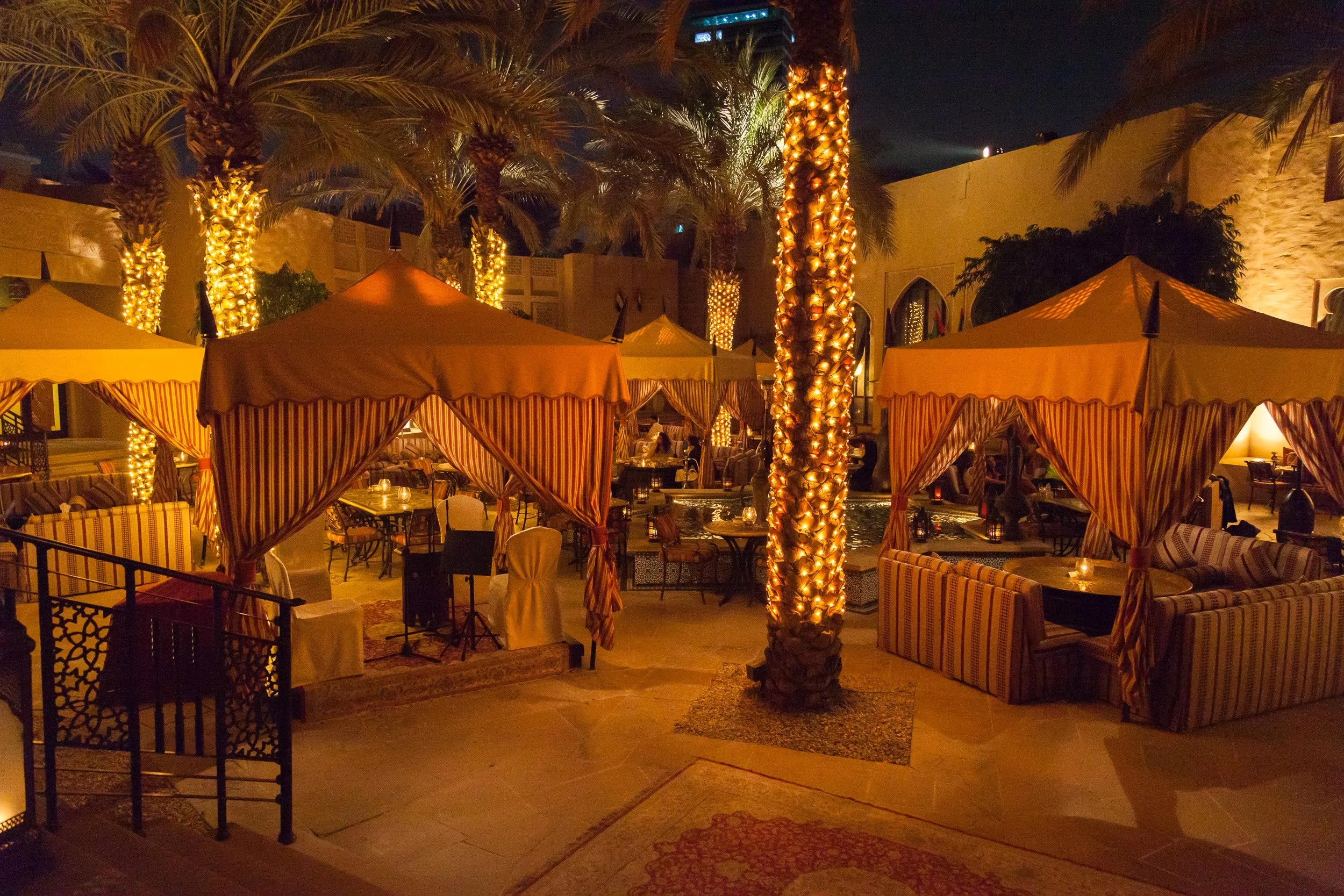 Palm-lit courtyards and striped tents creating an inviting Arabian evening setting in Dubai.