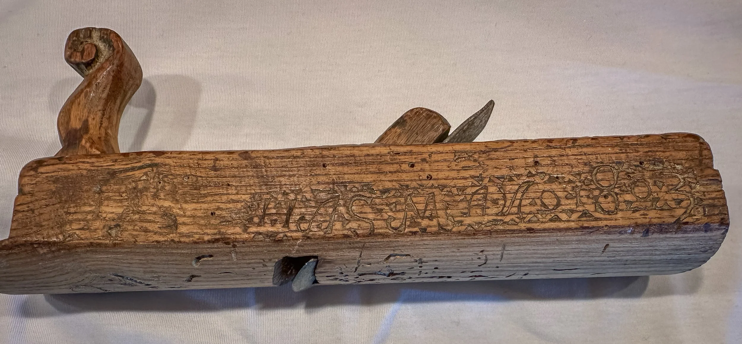 Motsatt side av en dekorert trehøvel med slitt innskrift, geometriske mønstre og et mulig årstall 1803.