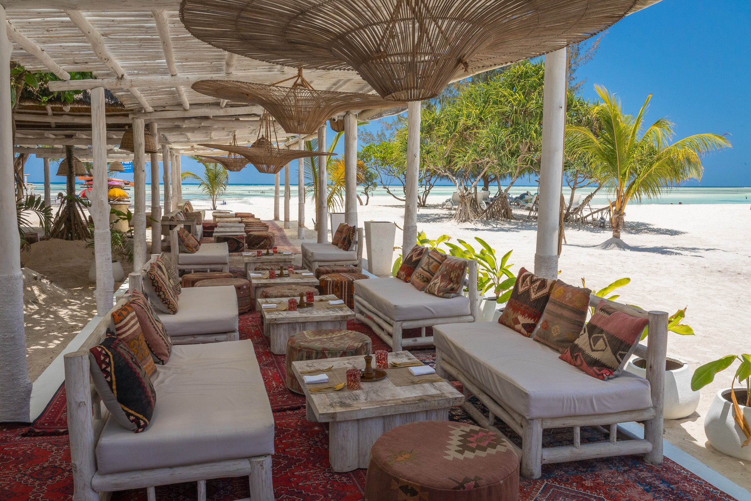 Outdoor restaurant at LUX Marijani, Zanzibar – open-air dining beneath wooden beams and palm fronds, overlooking the pool and Indian Ocean.