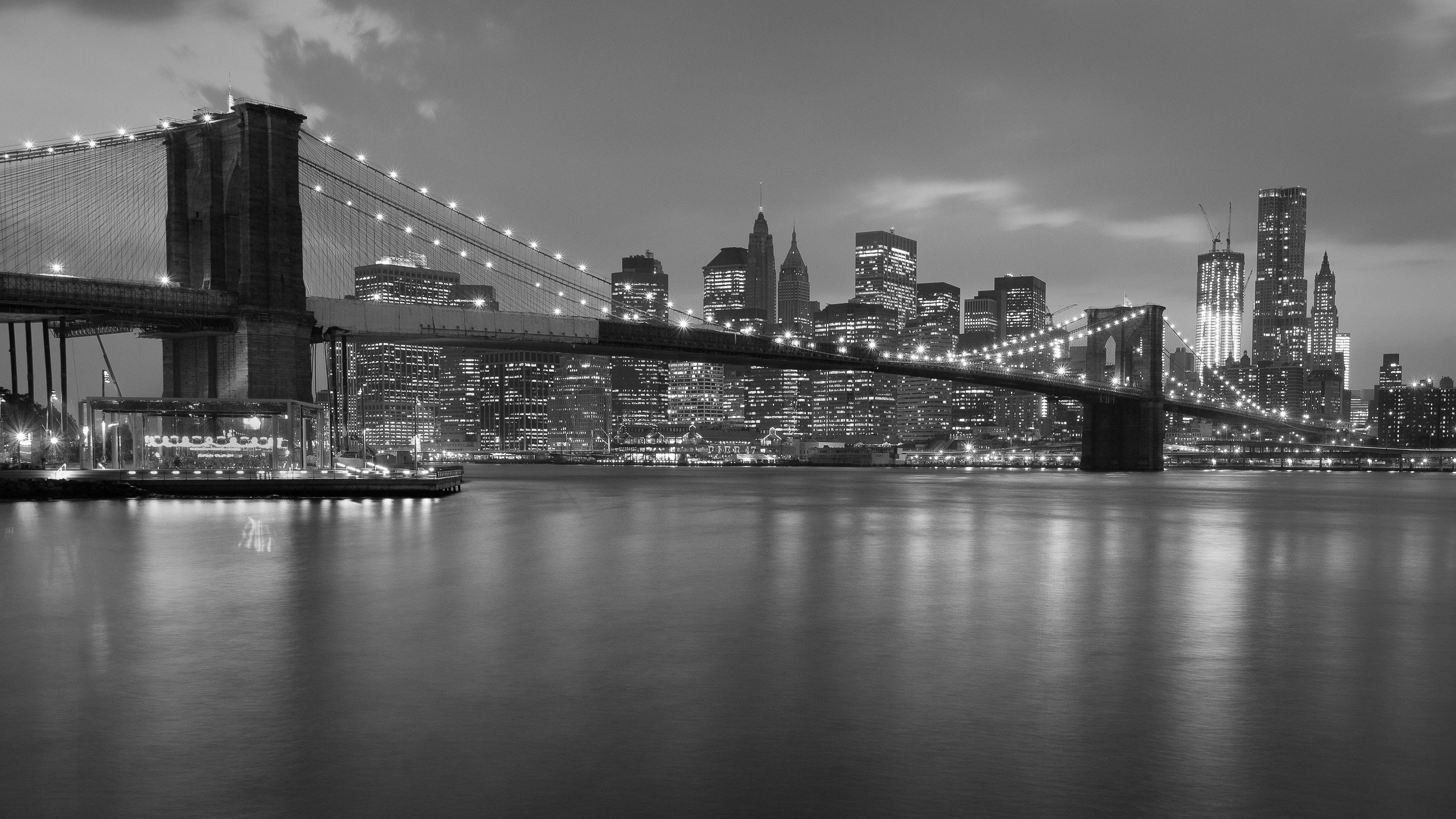 Brooklyn Bridge at blue hour, its lights leading the eye towards Manhattan’s glowing skyline.