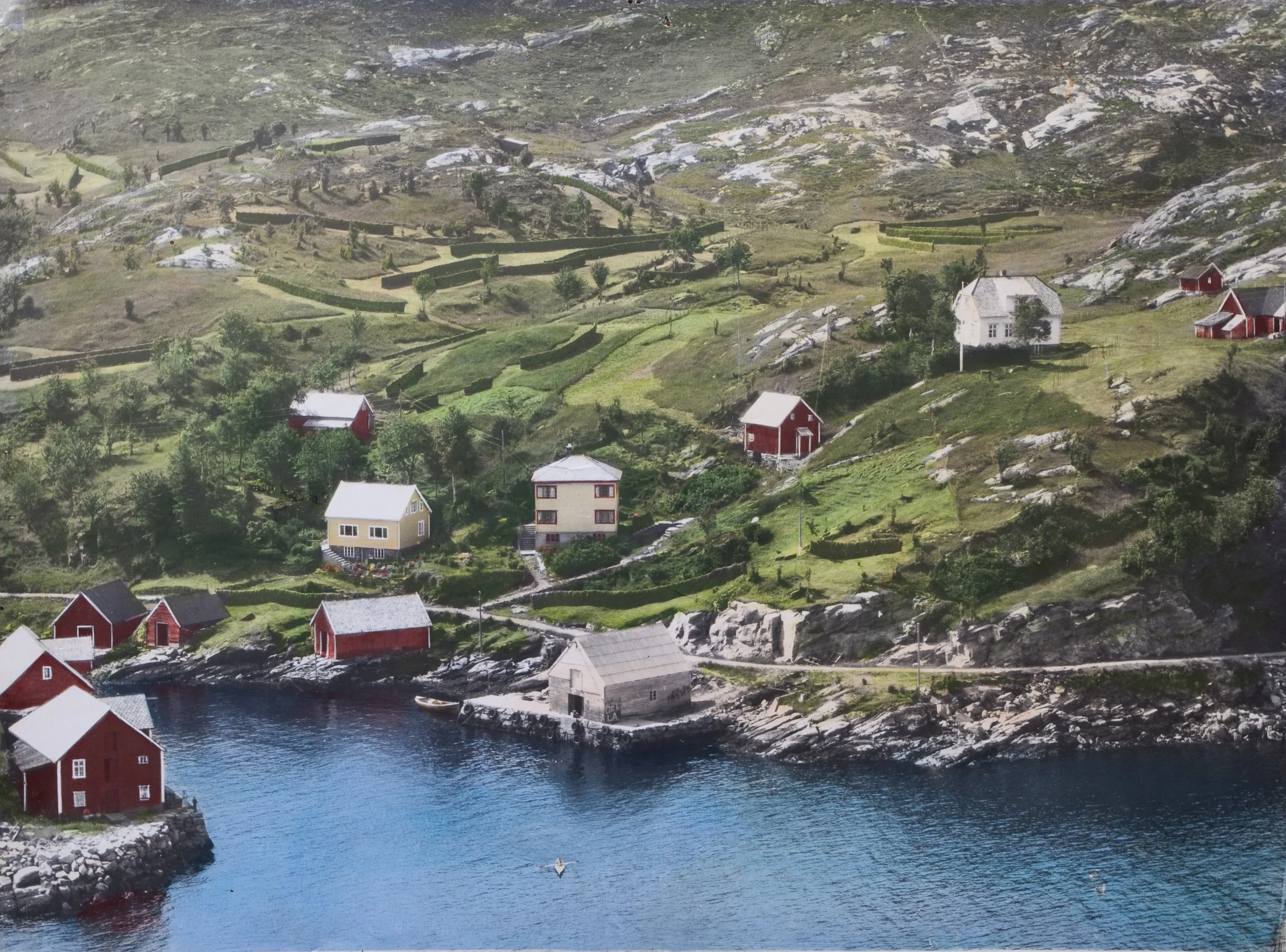 Vågen i Husevåg sett fra luften – historisk flyfoto som viser bygda, fjorden, sjøhusene, innmarka og fjellandskapet rundt Husevåg. Bildet gir et tydelig inntrykk av hvordan hus, små jordstykker, sjøhus og båtplasser lå tett sammen i et kystsamfunn de