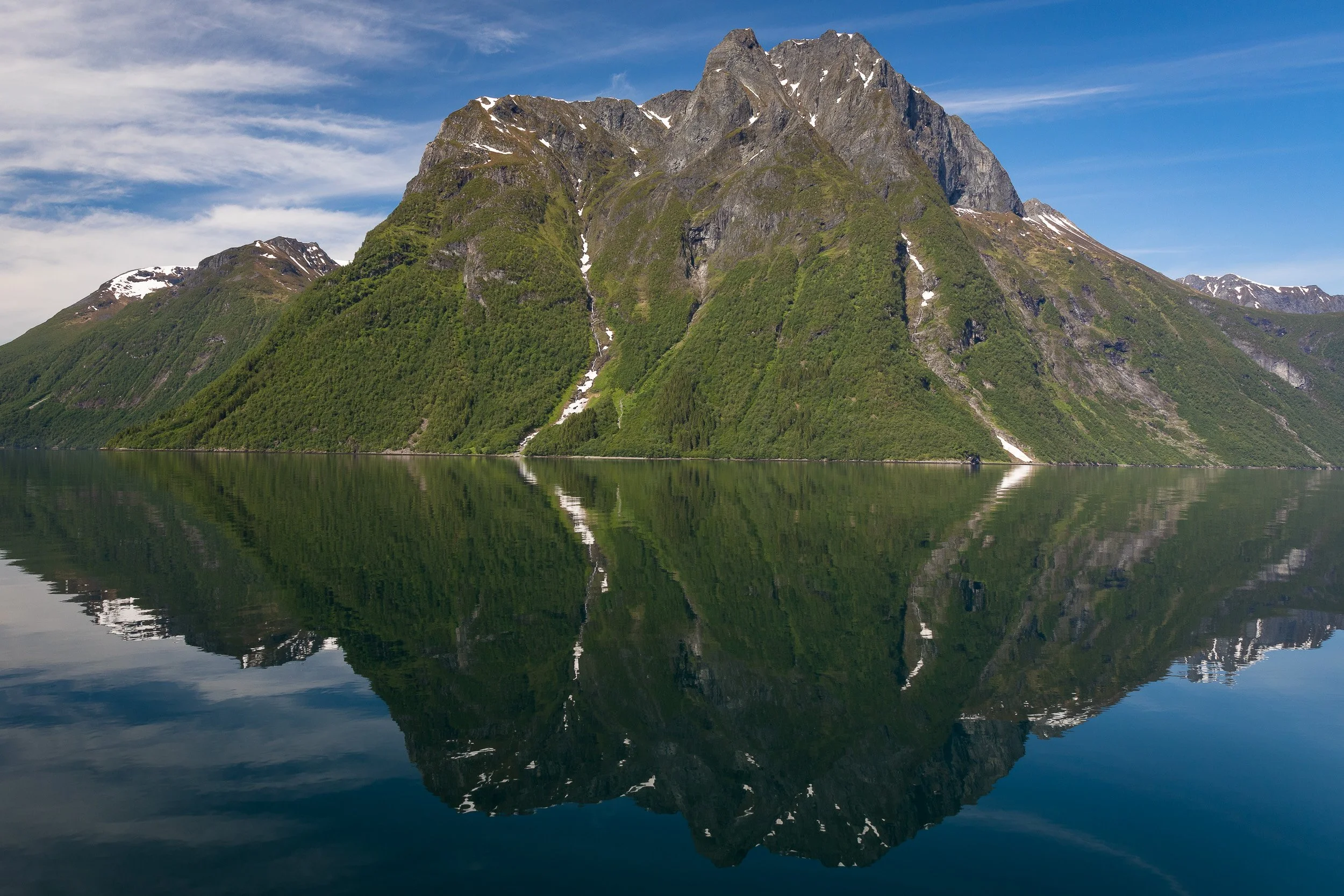 A peaceful shoreline scene in Hjørundfjorden, where reflections turn the fjord into a perfect, polished mirror.