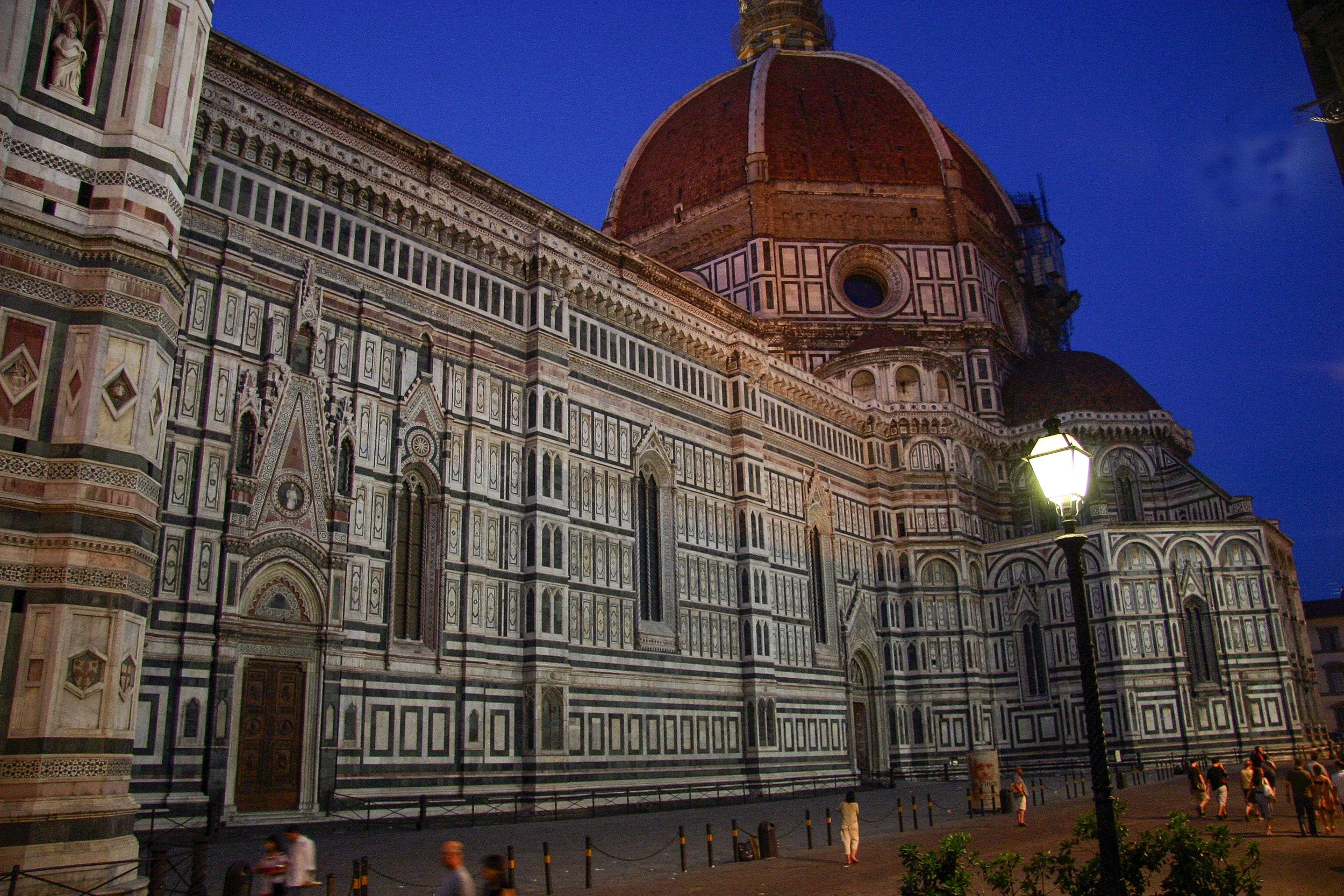 The marble geometry of Florence Cathedral at blue hour, lit by a single street lamp in the evening square.