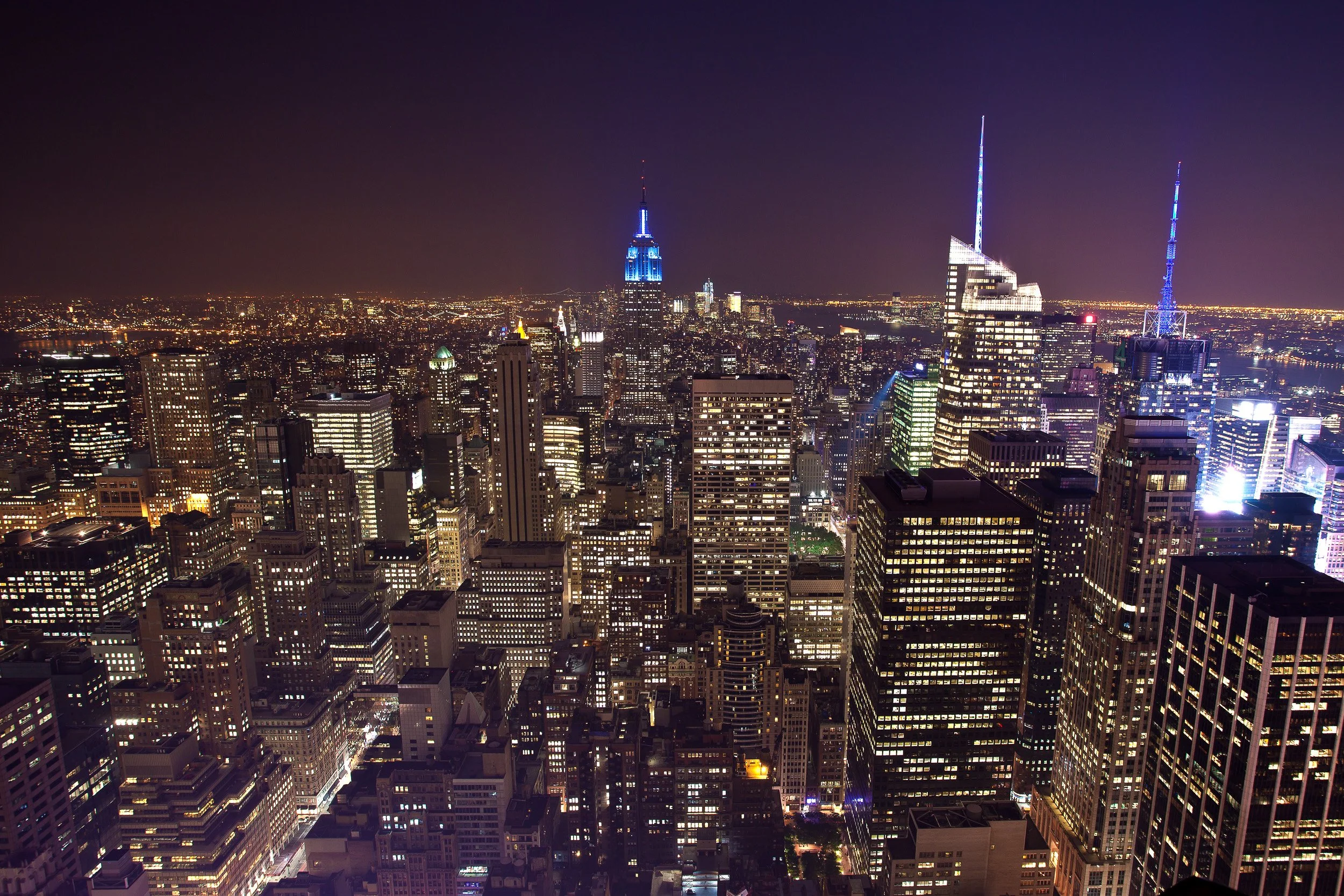 Manhattan after dark, a sea of lights stretching to the horizon with the Empire State Building glowing blue.