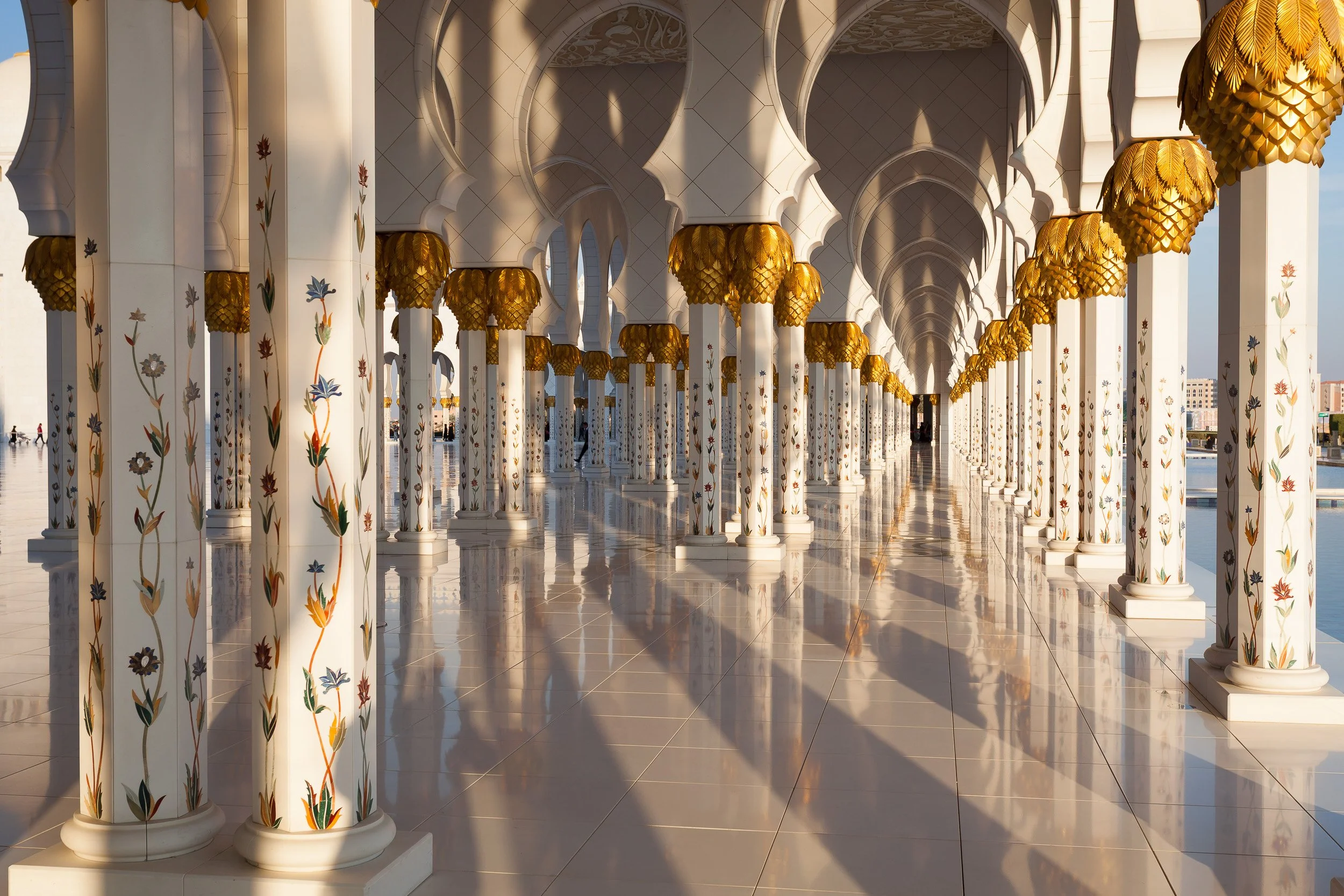 Floral columns and golden capitals leading the eye through the colonnade of Sheikh Zayed Grand Mosque, Abu Dhabi.