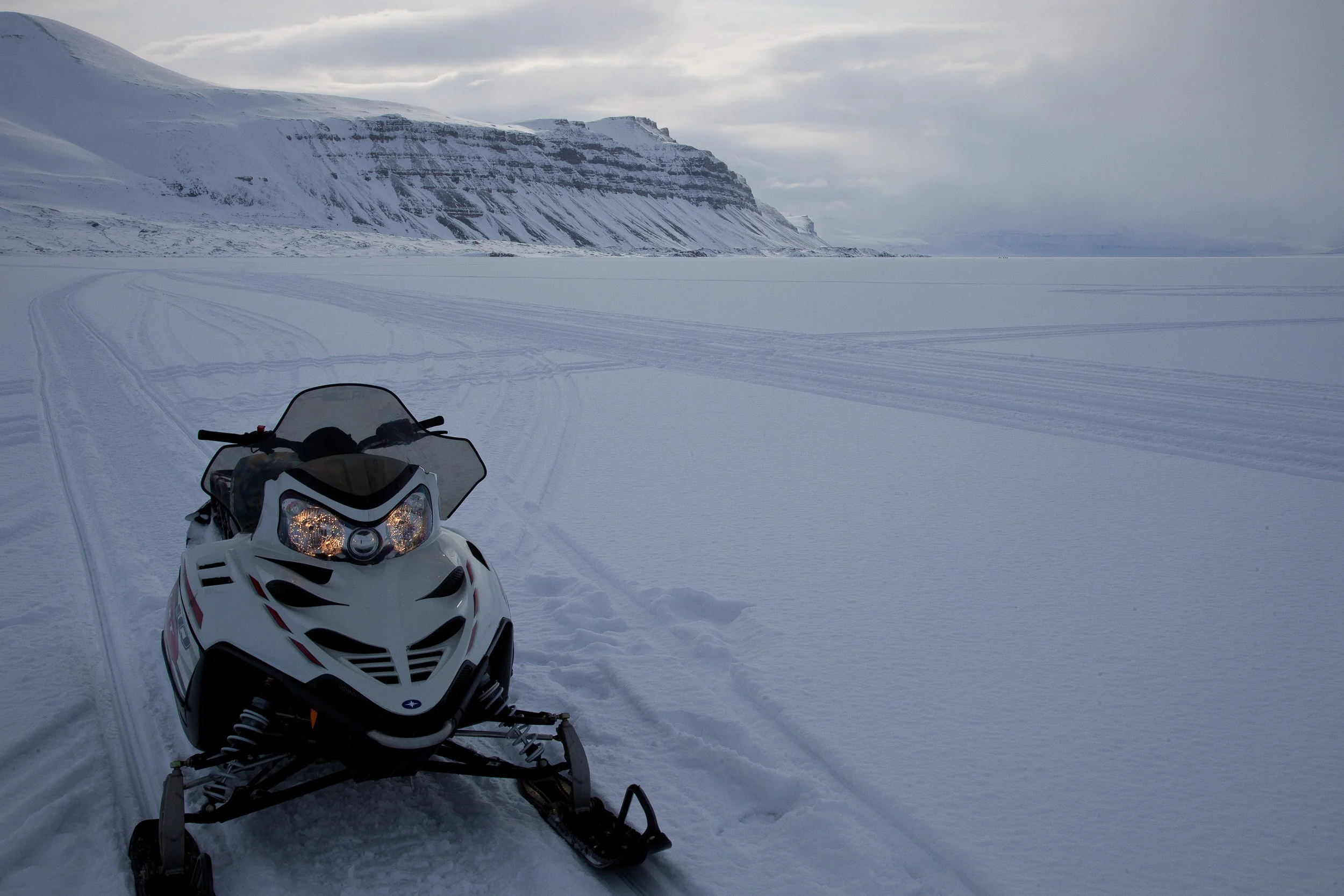 A snowmobile rests on the frozen fjord in Tempelfjorden, with tracks leading into the wide Arctic silence.