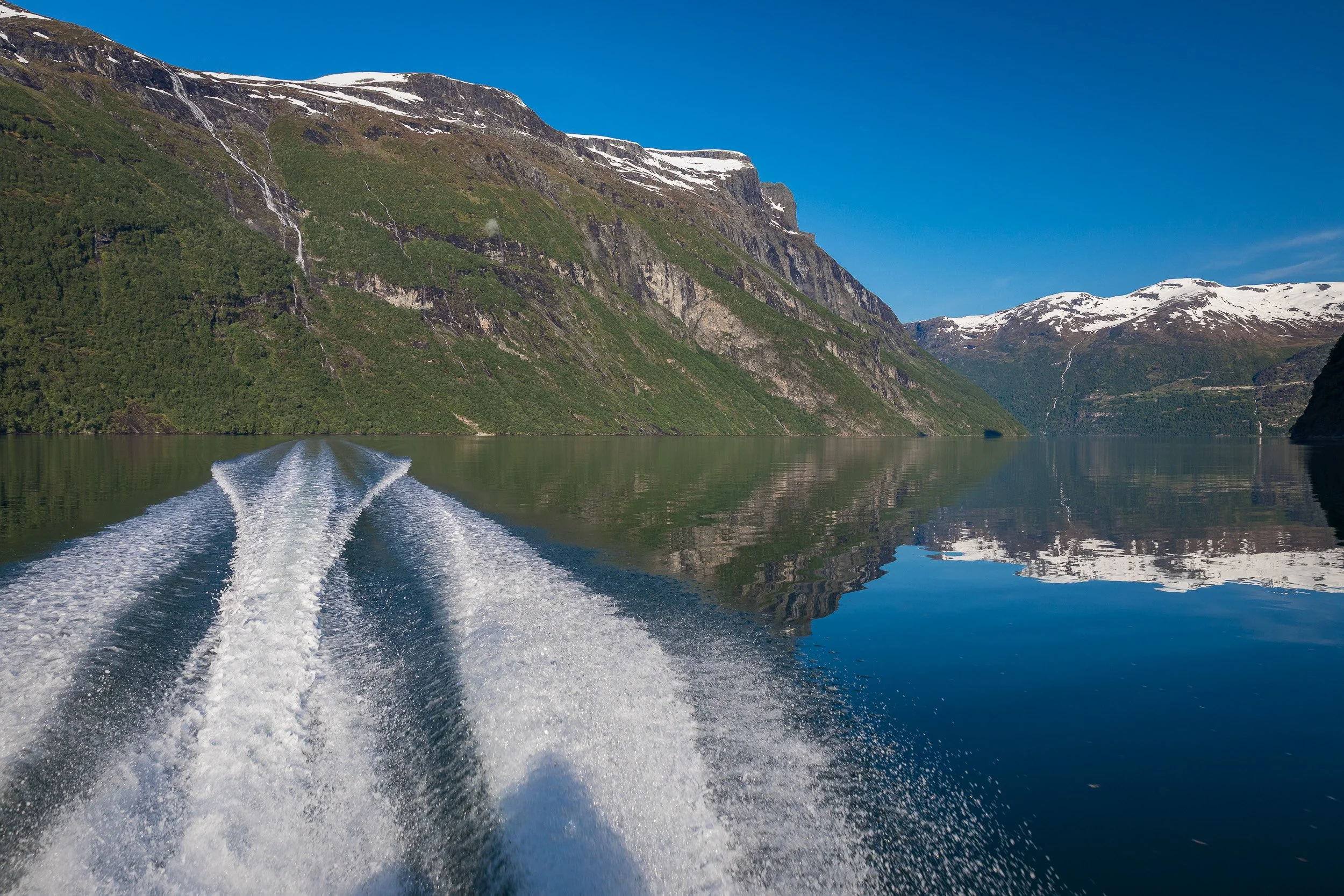 A swing floating out above Geirangerfjorden, with snow-streaked peaks beyond — pure fjord freedom in a single moment.