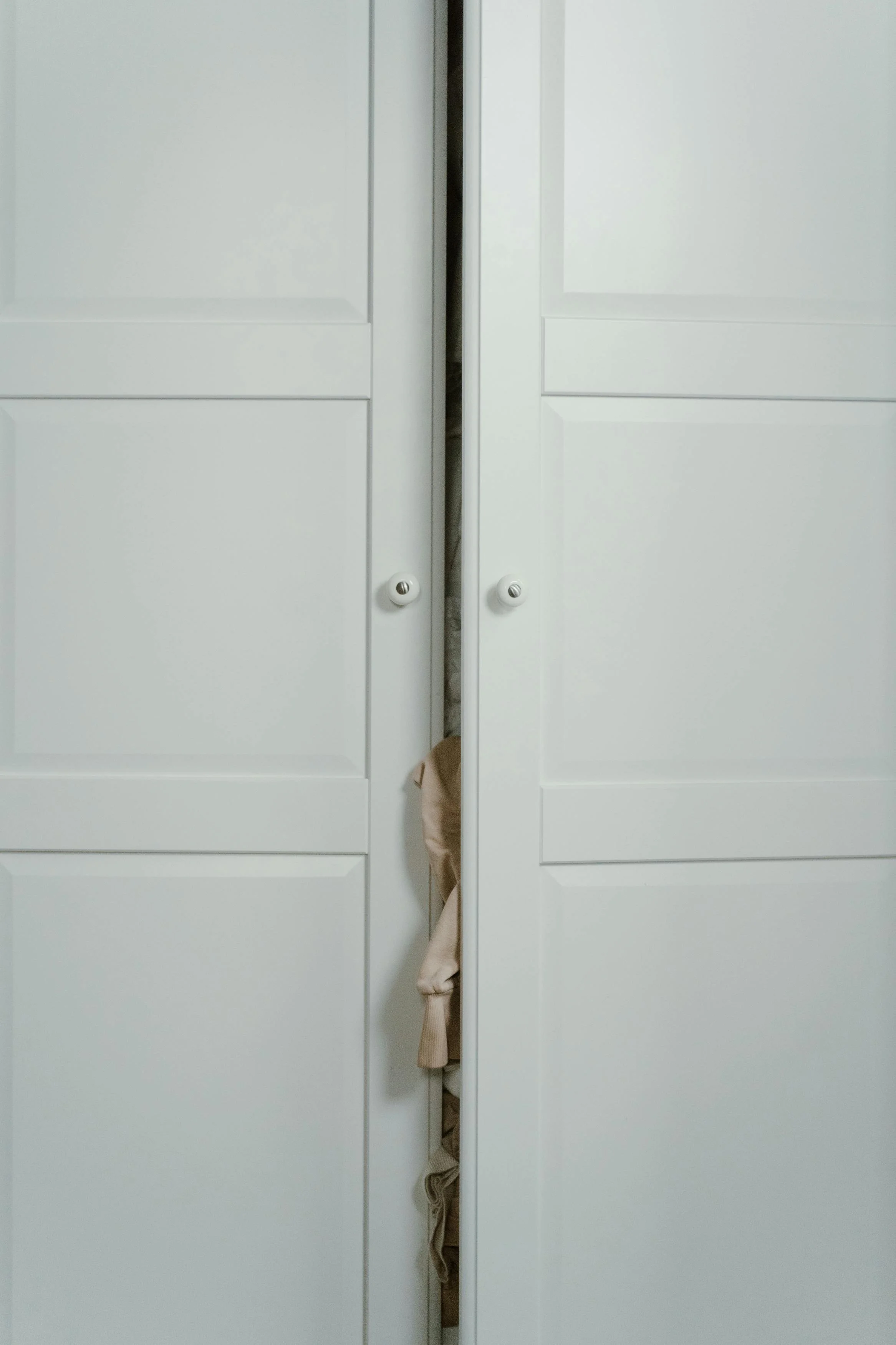 Minimalistischer Kleiderschrank mit leicht geöffneter Tür als Symbol für Kleiderschrankanalyse und -declutter und eine strukturierte Garderobe.